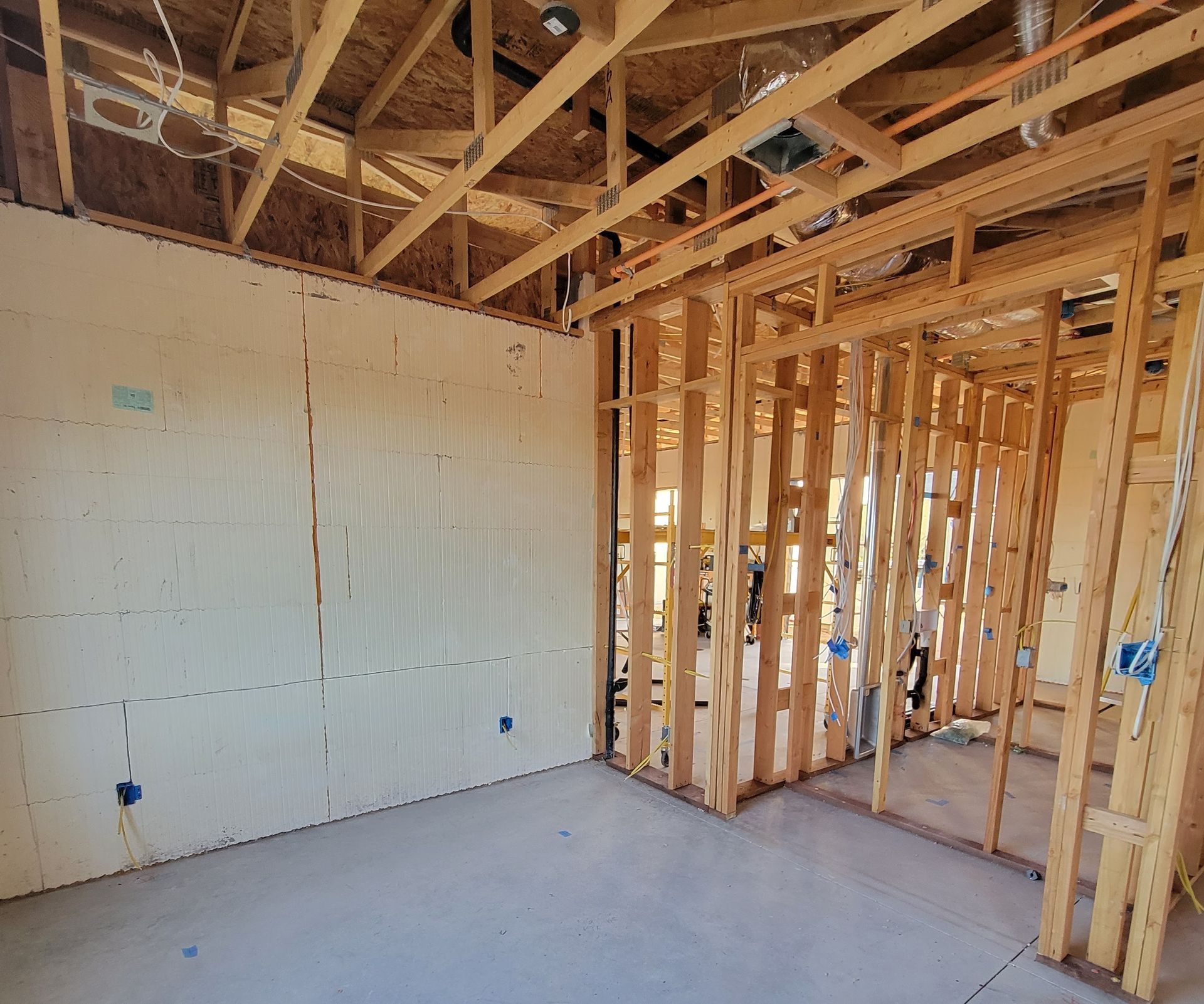 Interior of a room under construction, showing wooden framing, insulation, and concrete floor.
