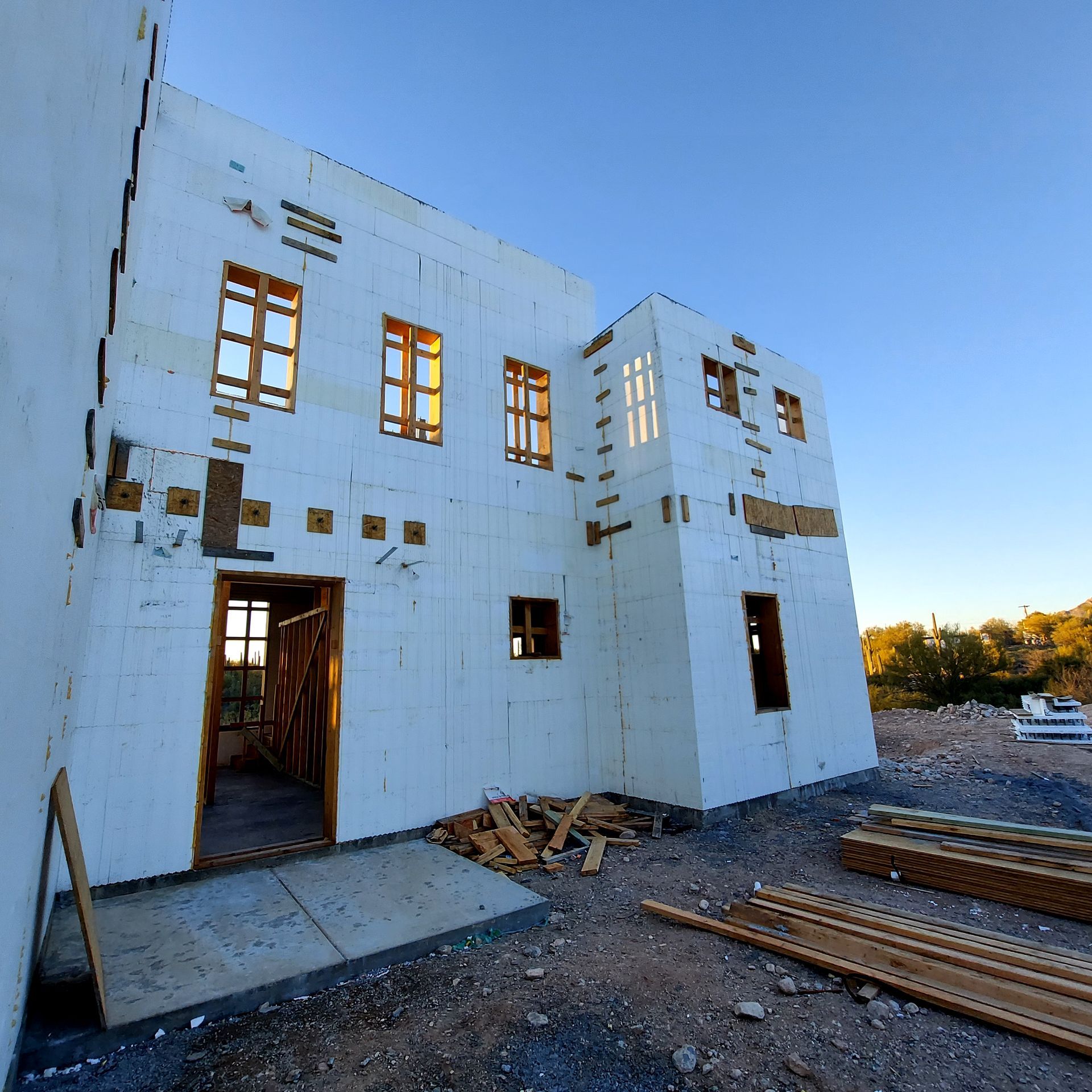 Building under construction, exterior view, with white foam panels, wooden window frames, and blue sky.