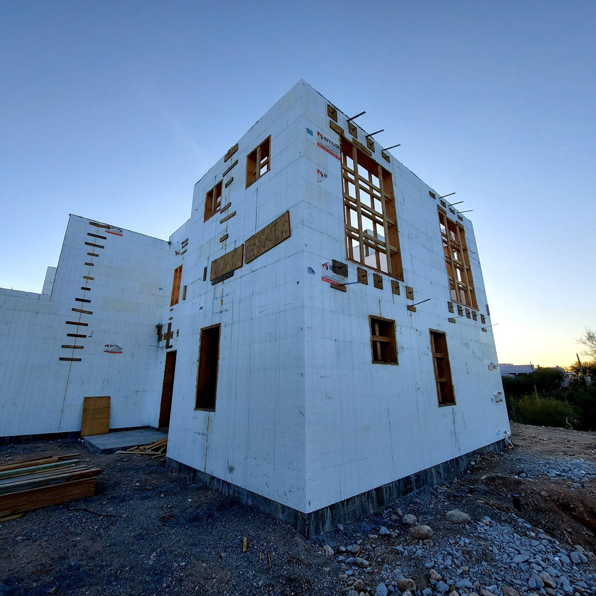 Exterior view of a two-story building under construction. White insulated concrete form walls, window openings, clear sky.