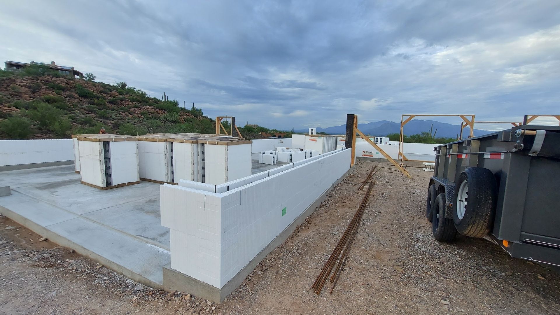 Construction site with white ICF blocks forming walls, on a concrete foundation, outdoors under cloudy sky.