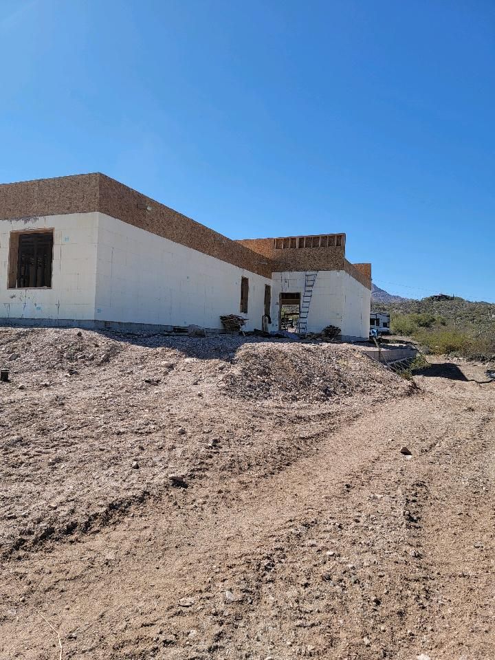 Building under construction on a dirt lot; white walls, brown trim under clear blue sky.