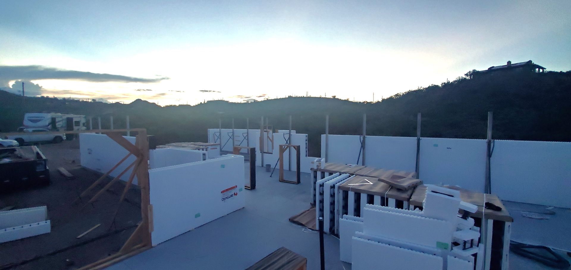Construction site with insulated concrete forms, set against a backdrop of a mountain under a sunset sky.