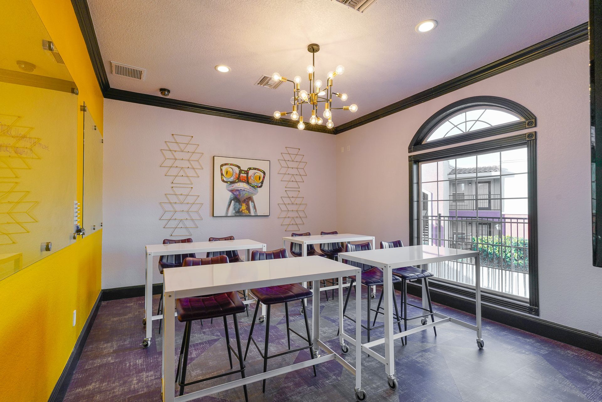 A bright room with tables, chairs, and a window. Artwork on the walls, chandelier lighting.