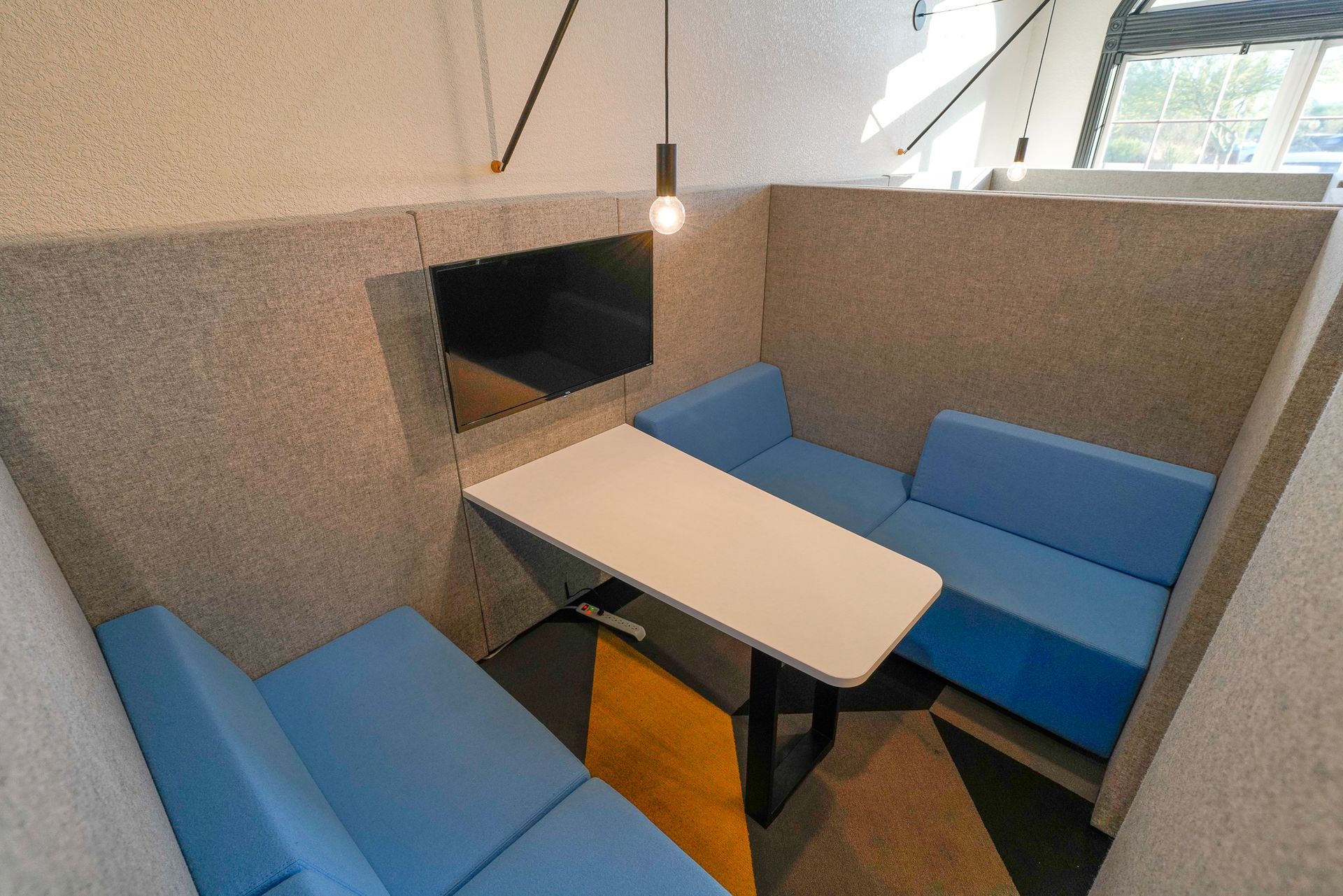 Acoustic office booth with blue seating, white table, and a mounted TV.