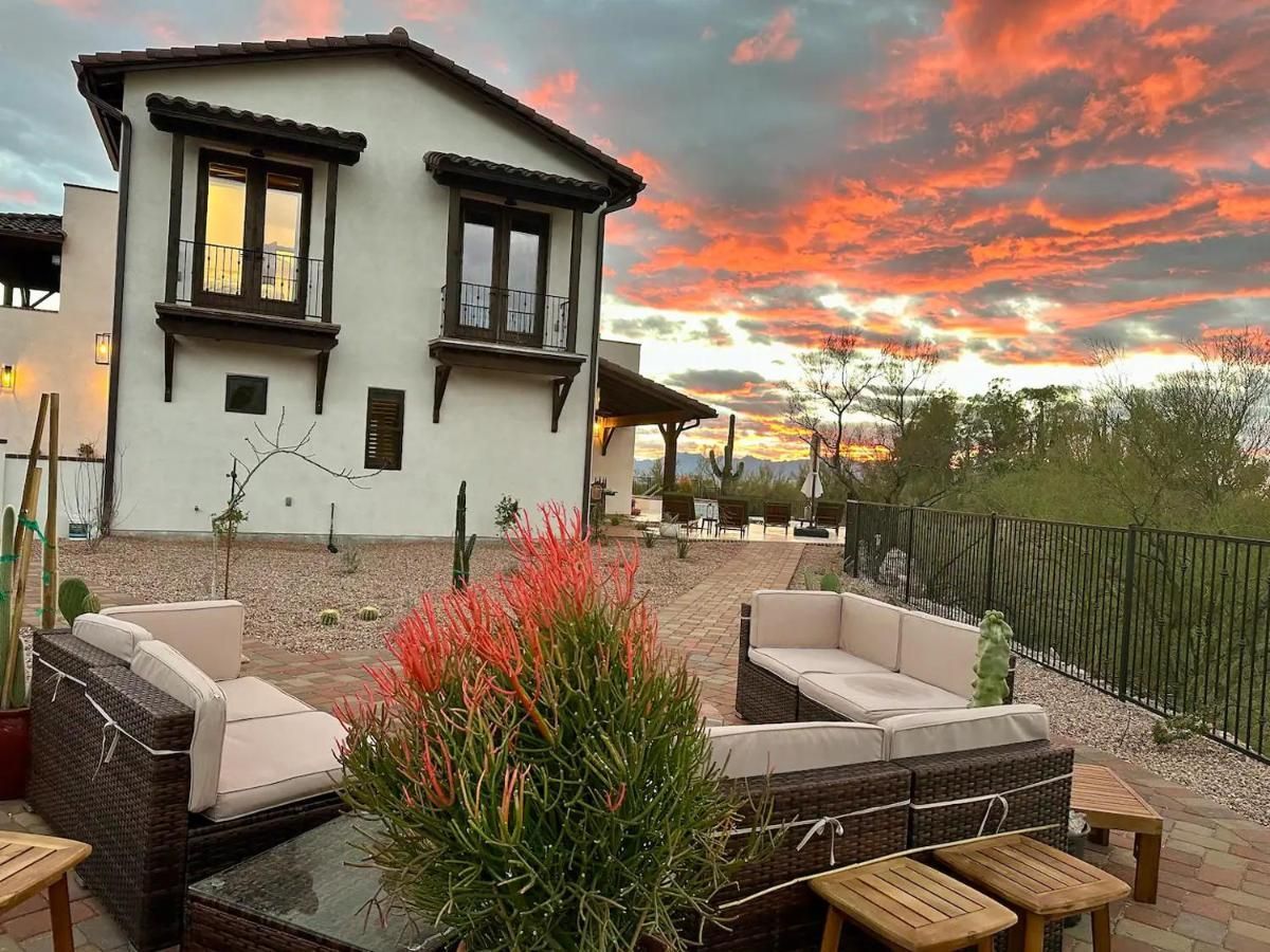 Patio seating in front of a stucco building; sunset with orange and pink clouds.