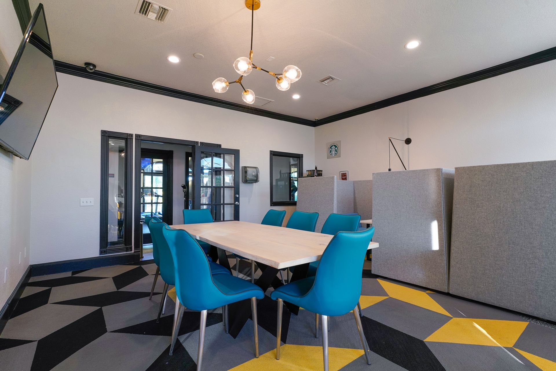 Conference room with teal chairs, white table, geometric carpet, and a gold chandelier.