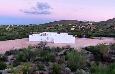 A large white building in the middle of a desert surrounded by trees and bushes.