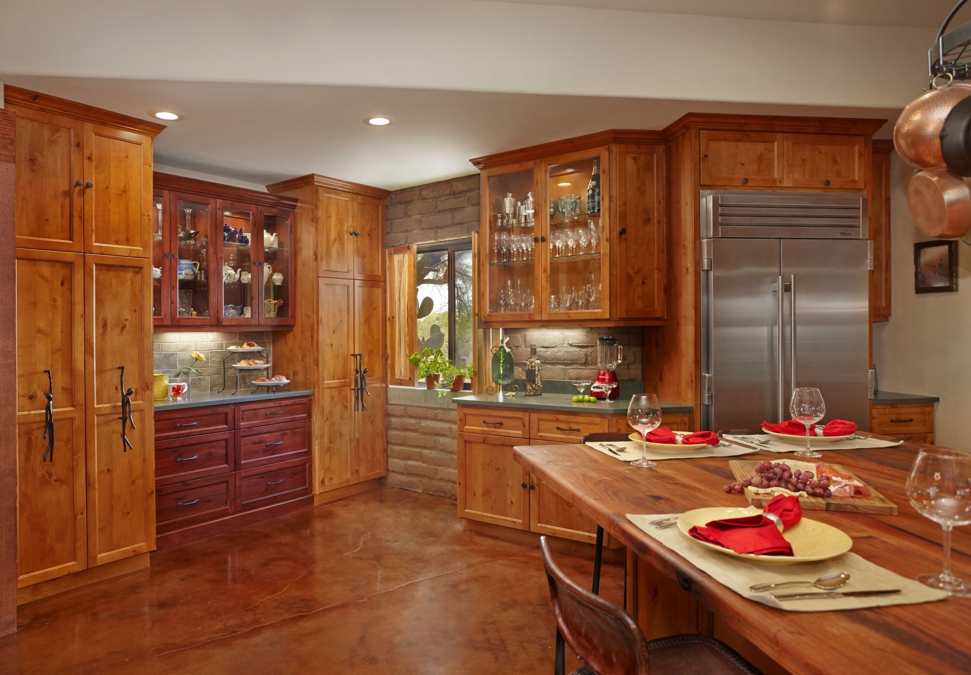 Rustic kitchen with wood cabinets, stainless steel refrigerator, and a large wooden island with place settings.