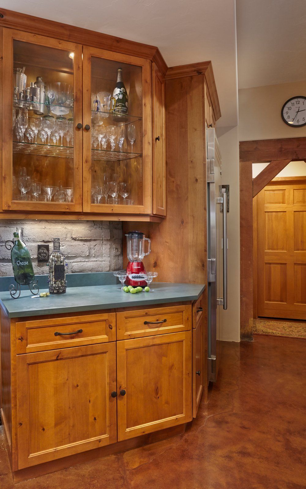 Wooden kitchen cabinets with glassware and a blender. A refrigerator and doorway are adjacent.
