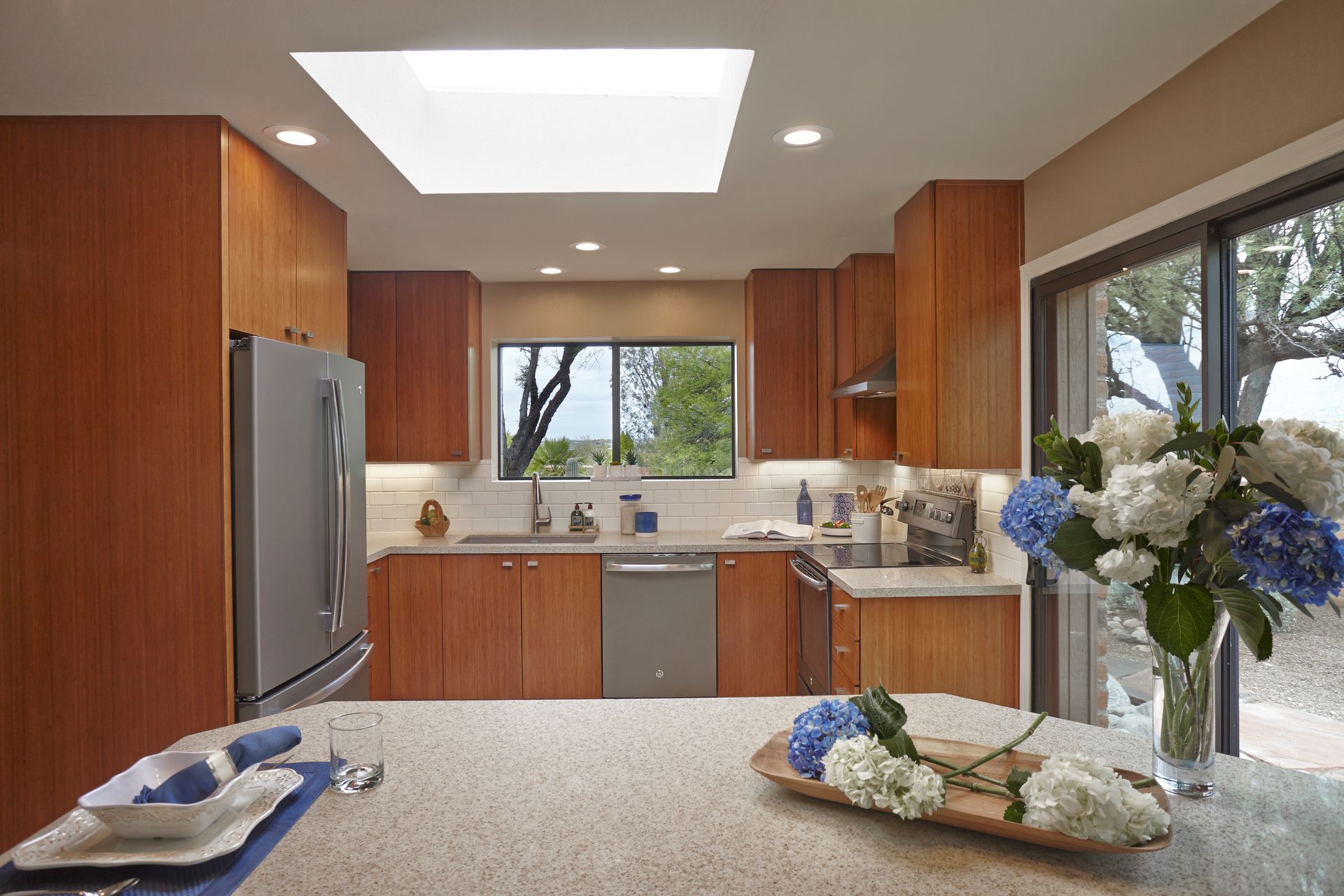Modern kitchen with wood cabinets, stainless steel appliances, and skylight. Flowers on a countertop.