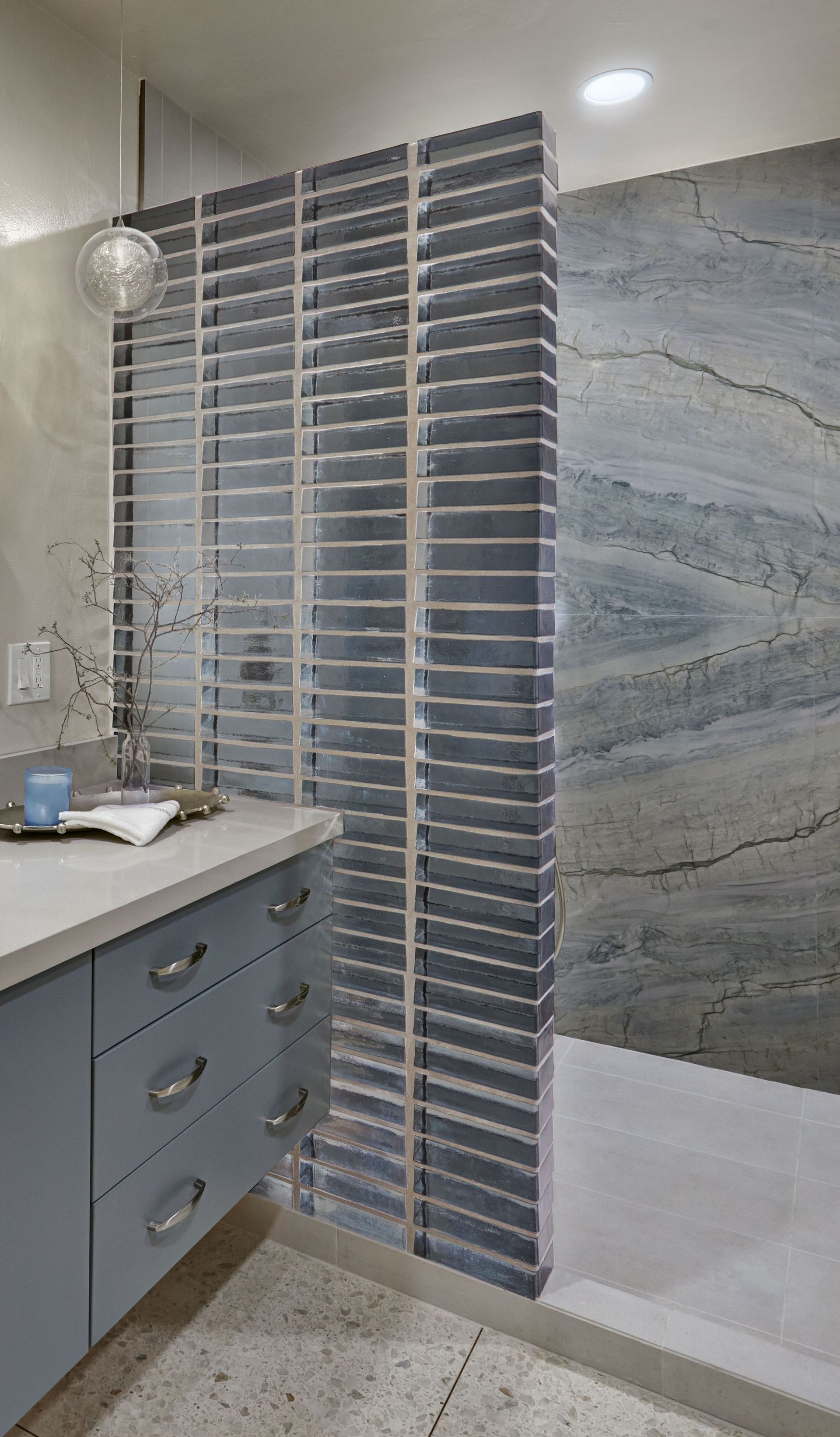 Bathroom with gray cabinets, a tiled shower divider, and blue stone shower wall.