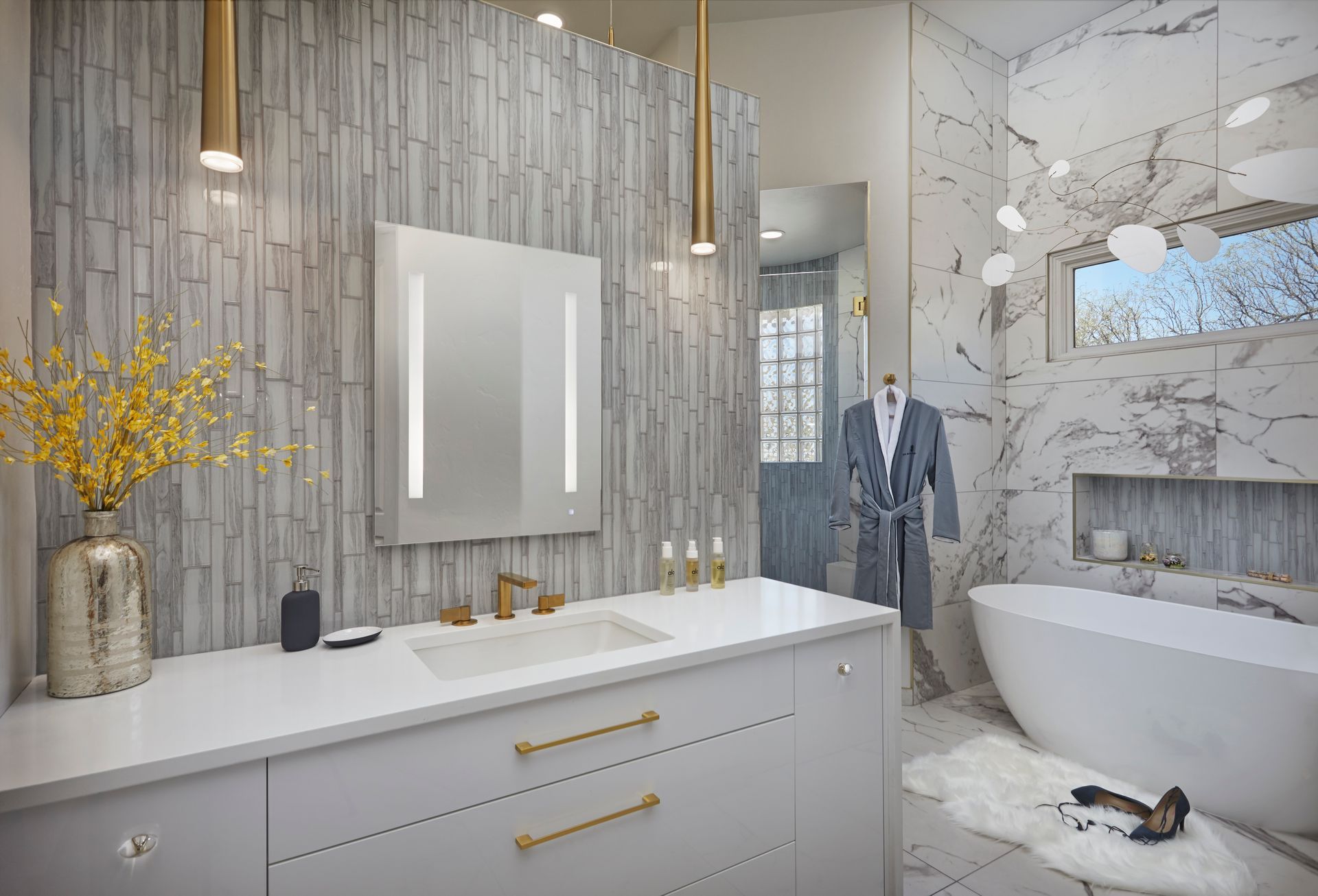 Modern bathroom with marble and textured tile, white vanity, gold fixtures, and a freestanding tub.
