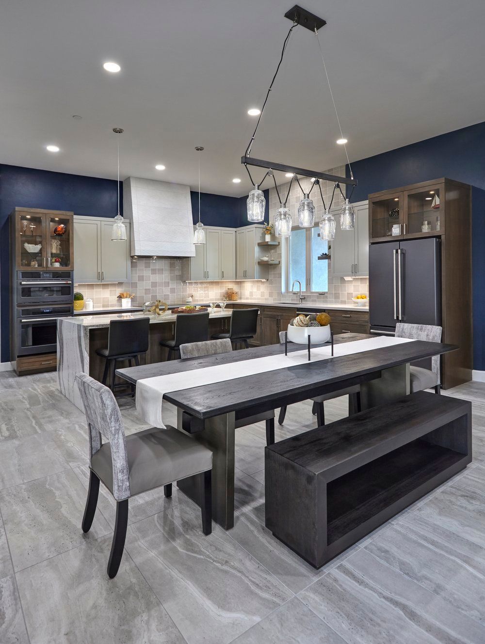 Modern kitchen and dining area with dark wood table and bench, gray chairs, and blue walls.