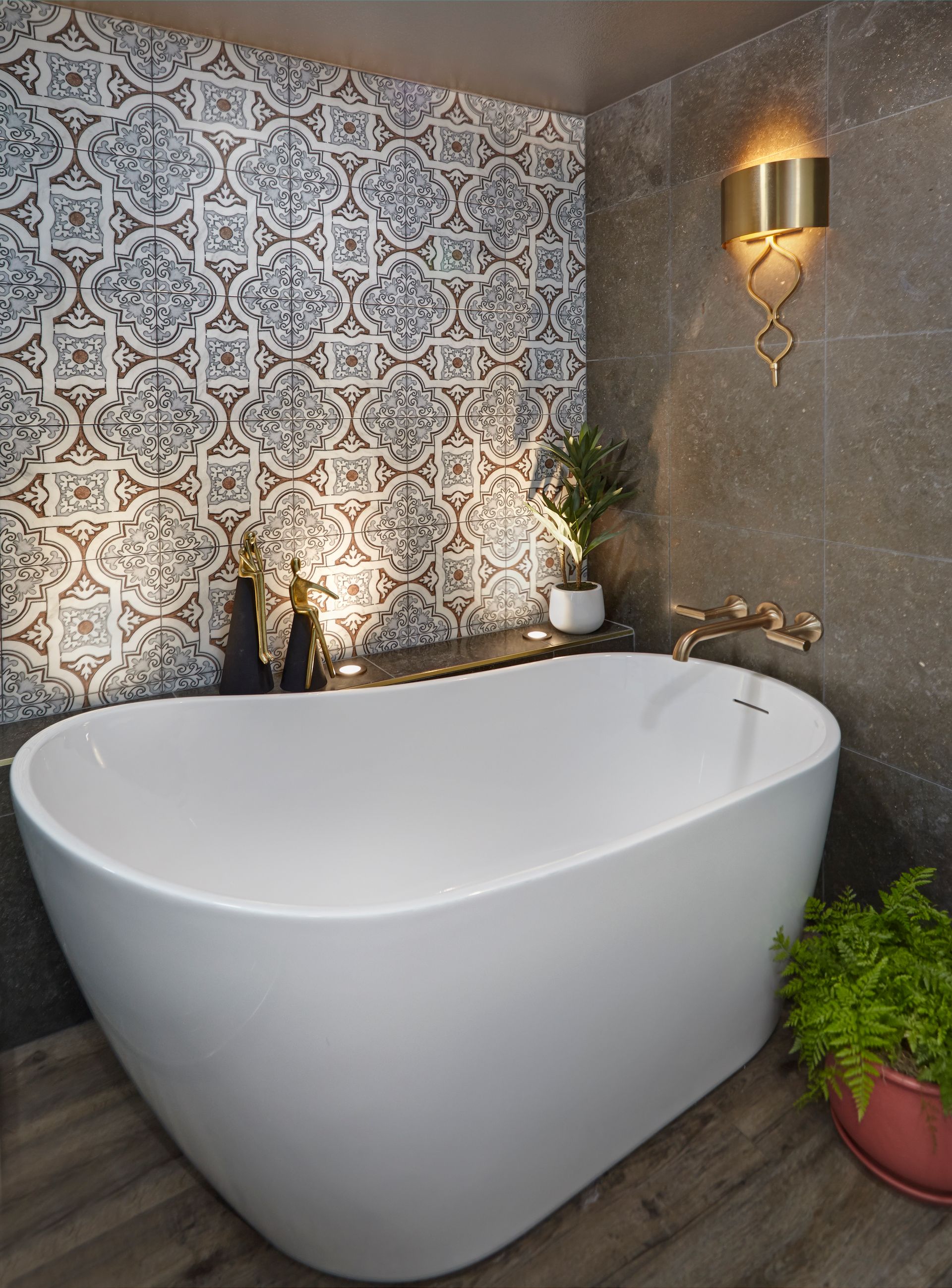 Modern bathroom with white freestanding tub, patterned wall tile, brass fixtures.
