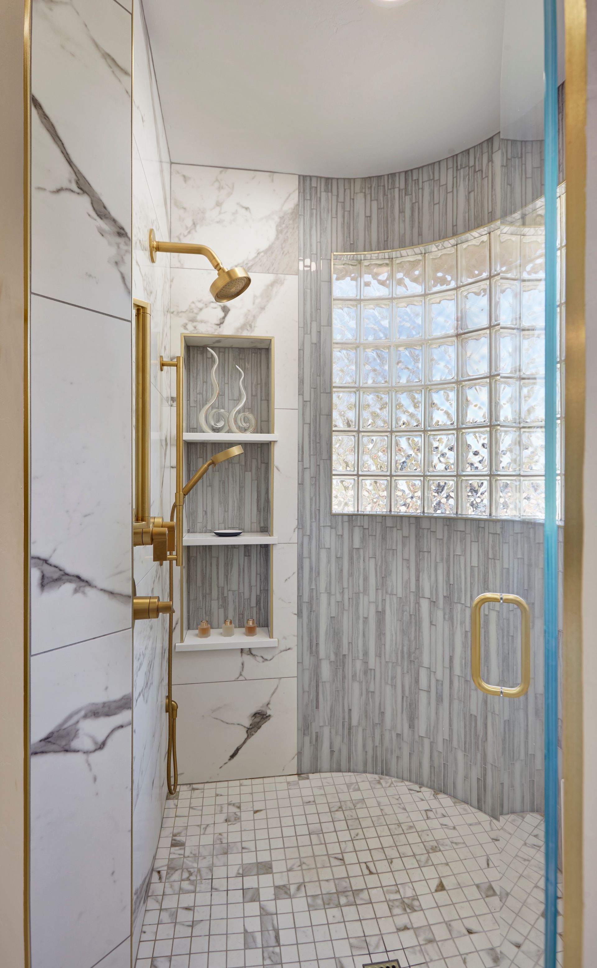 Luxurious shower with gold fixtures and marble accents. Glass block window.