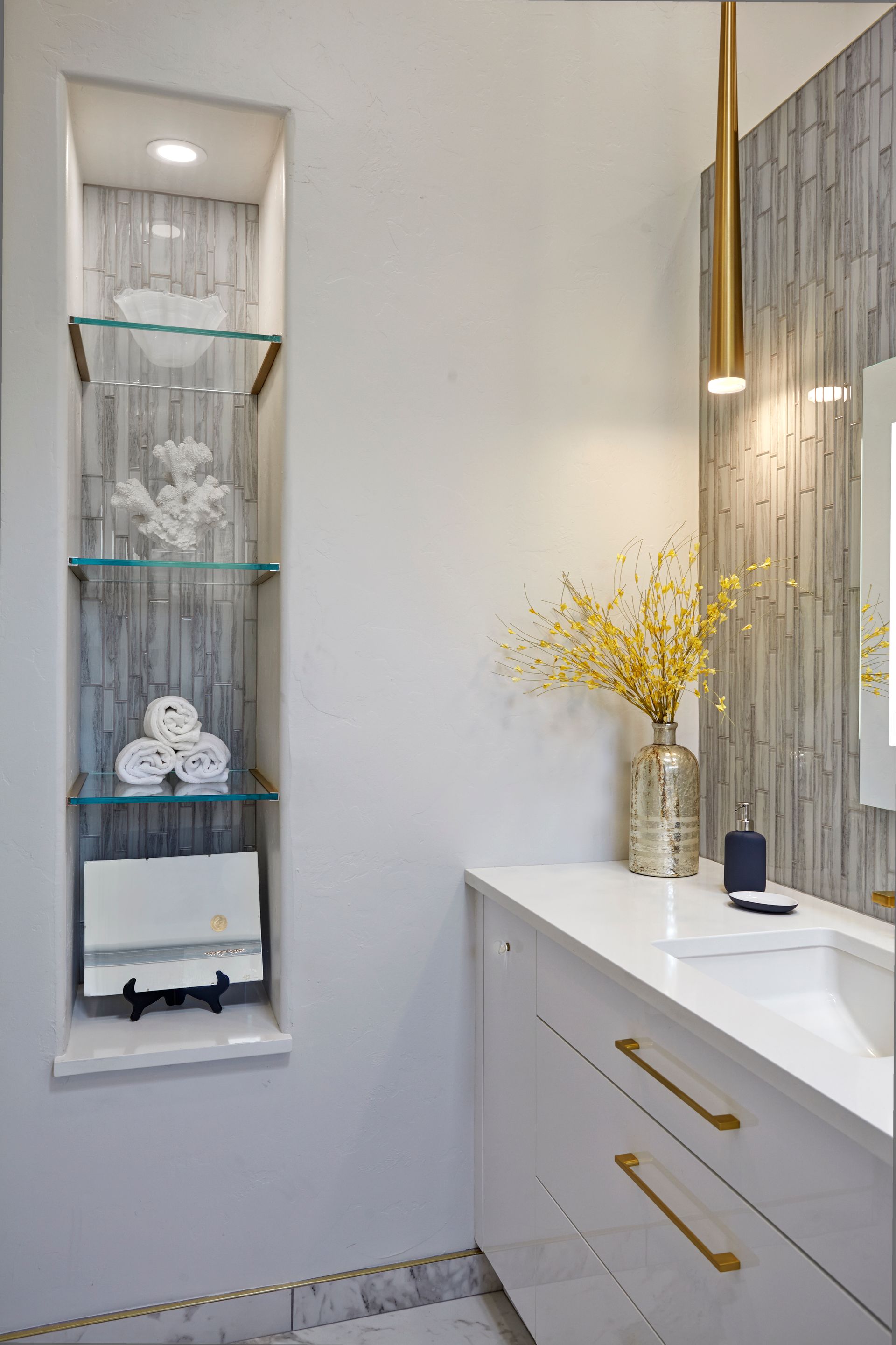 Bathroom with recessed shelves holding decor, white vanity, and gold accents.