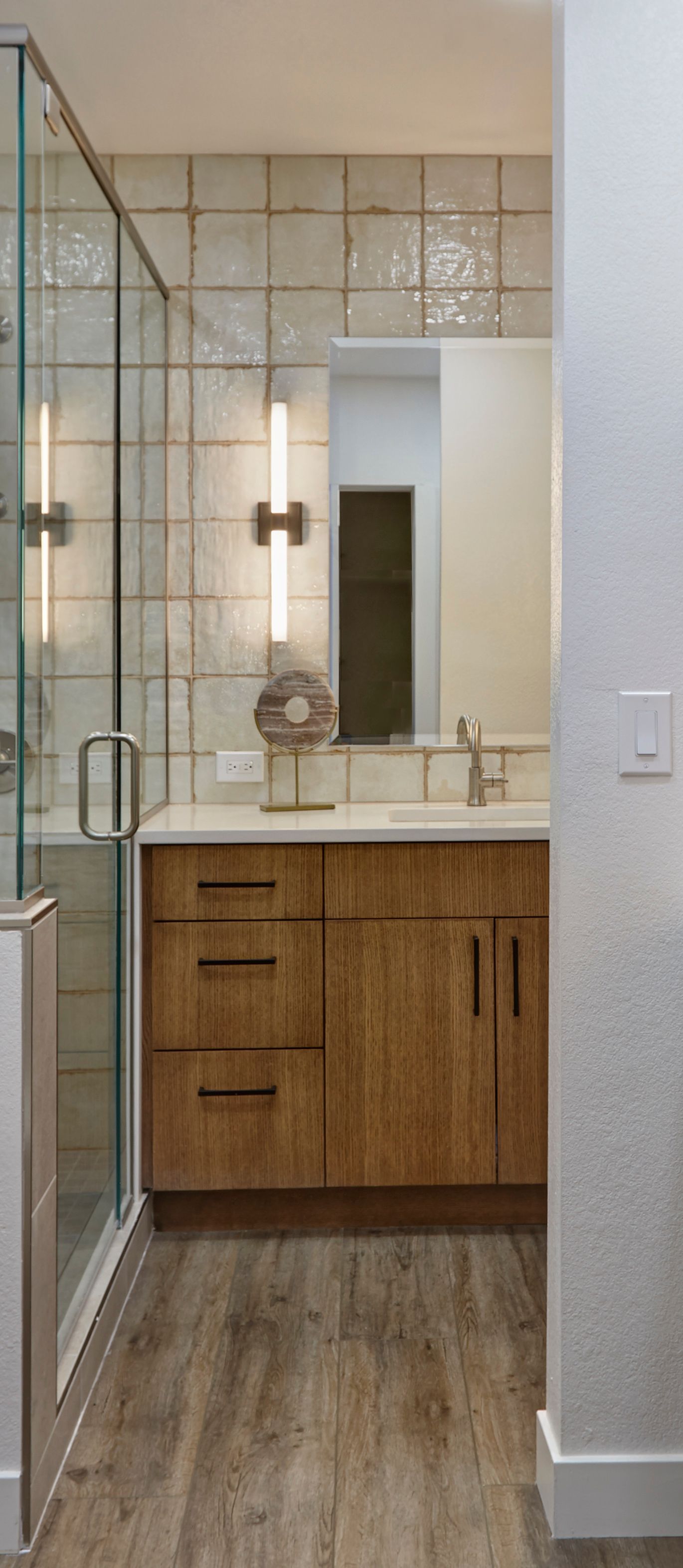 Bathroom with a wooden vanity, a glass shower, and patterned wall tile.