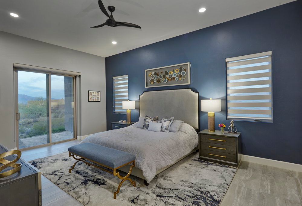 Bedroom with blue accent wall, large bed, gray rug, and sliding door.