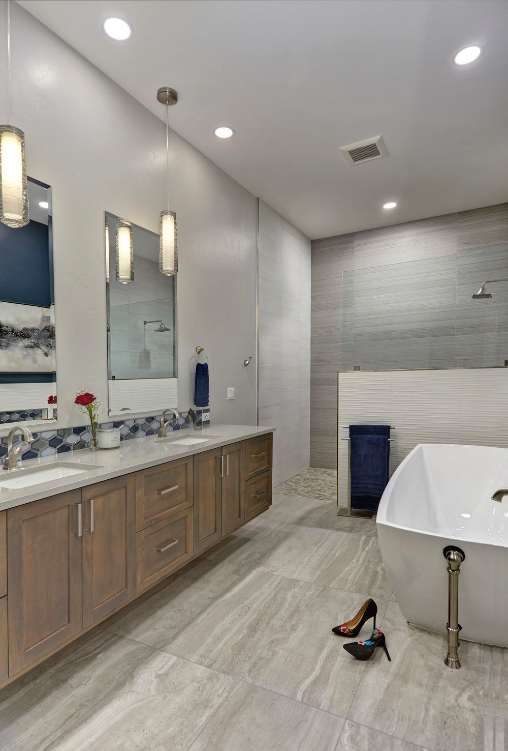 Modern bathroom with wood vanity, large tub, stone tile, and gray and blue accents.