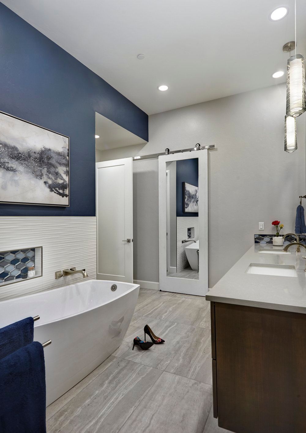 Modern bathroom with a white tub, blue accent wall, and wood vanity.