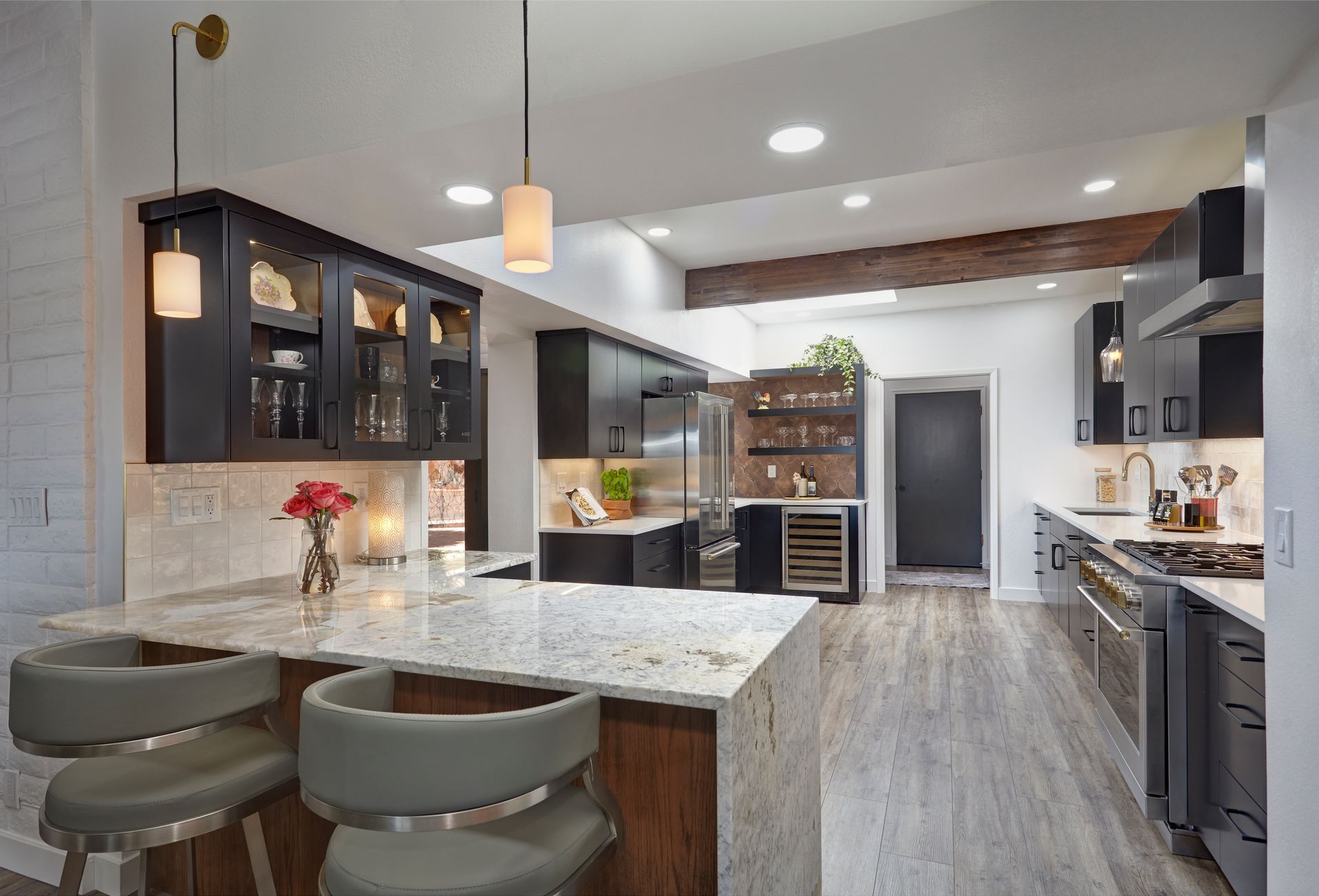 Modern kitchen with granite island, dark cabinets, stainless steel appliances, and wooden beam.