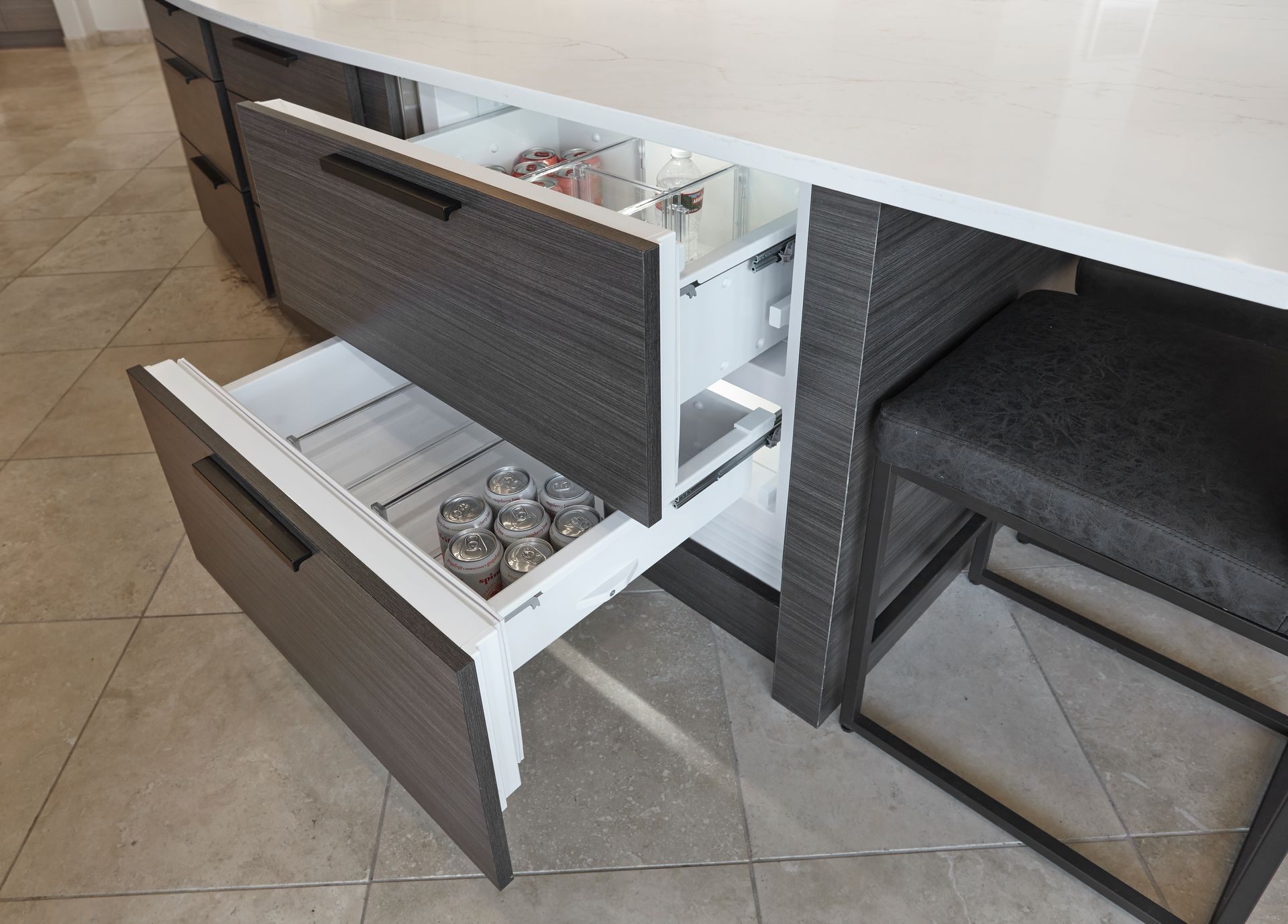 Kitchen island with two pull-out drawers, one open with glassware, other open with a small refrigerator.