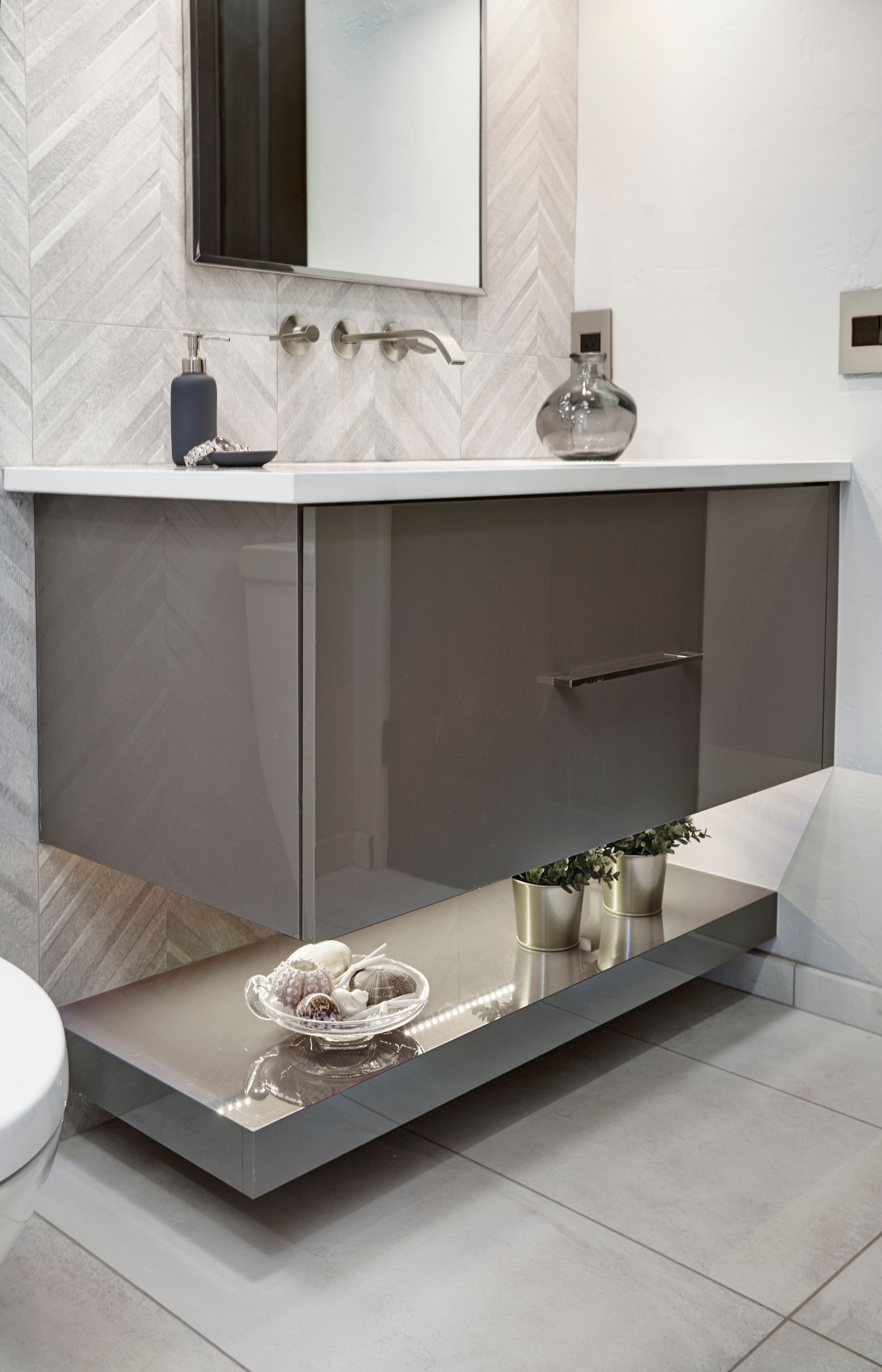 Modern gray bathroom with floating vanity, shelf, and herringbone backsplash.