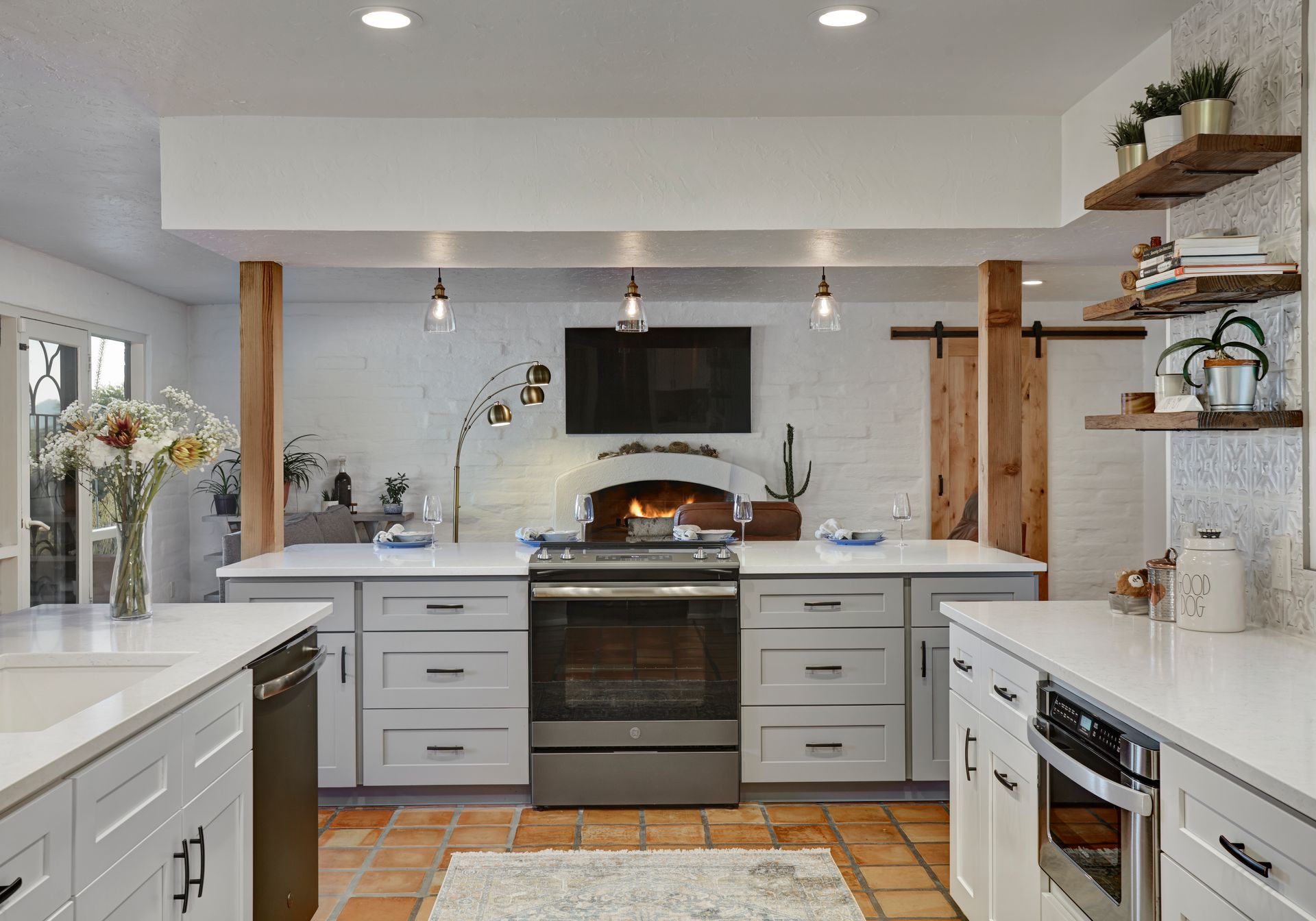 A kitchen with a stove, white cabinets, and a terracotta tile floor. Exposed wood beams and shelving.
