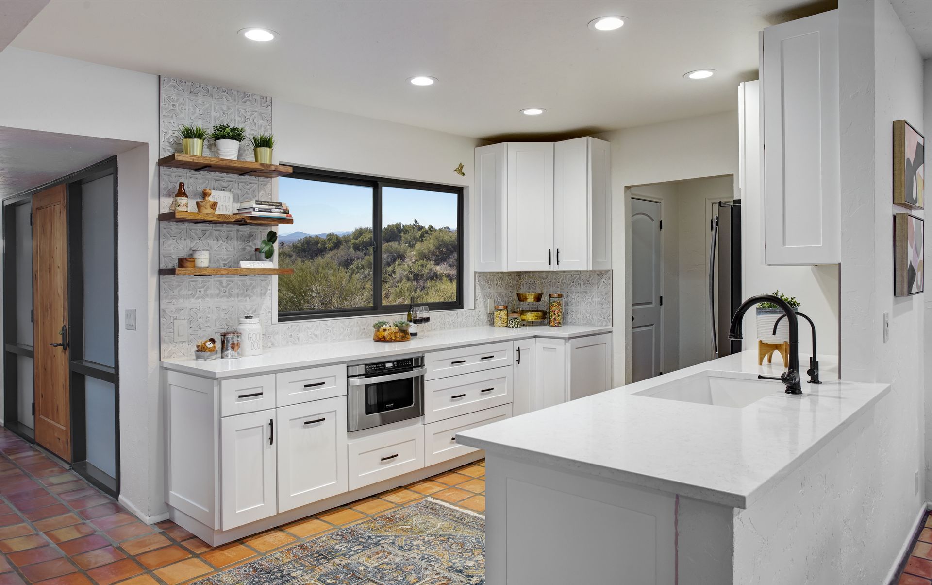 White kitchen with a large window, white countertops, and open shelving.