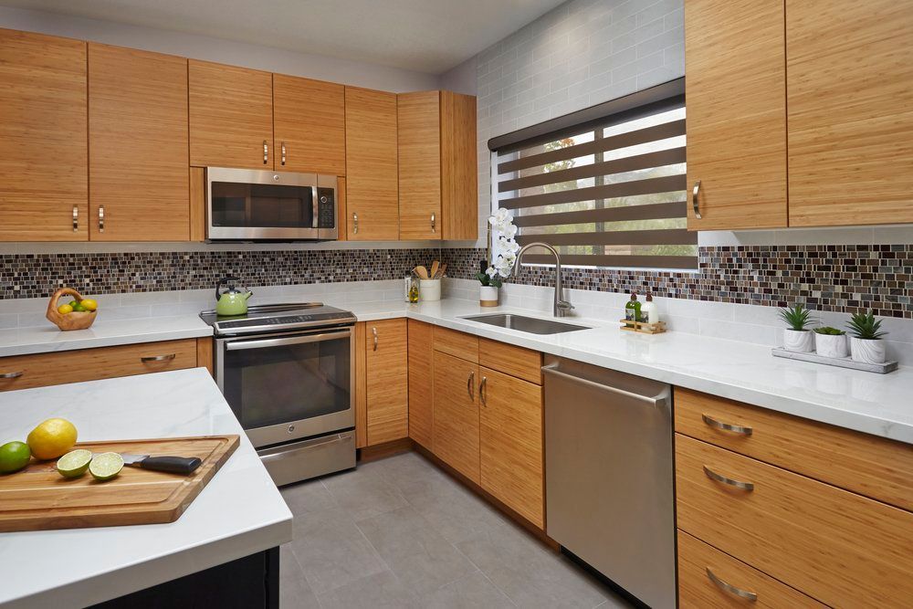 A modern kitchen with light wood cabinets, stainless steel appliances, white countertops, and a mosaic backsplash.