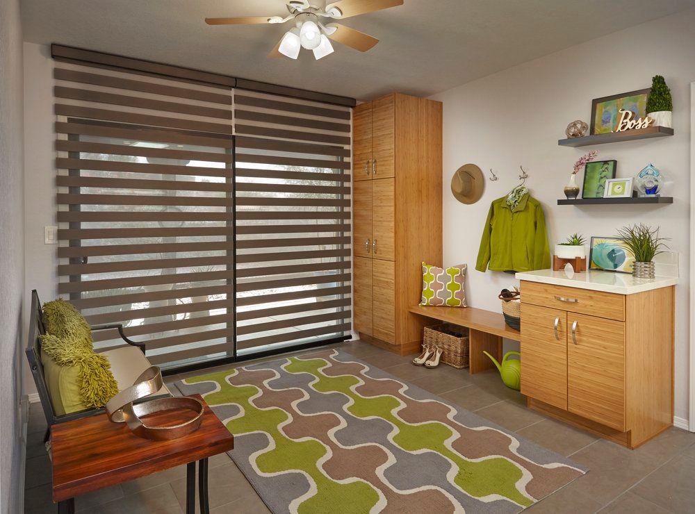 A well-lit, organized mudroom with storage cabinets, bench, patterned rug, and brown horizontal blinds.