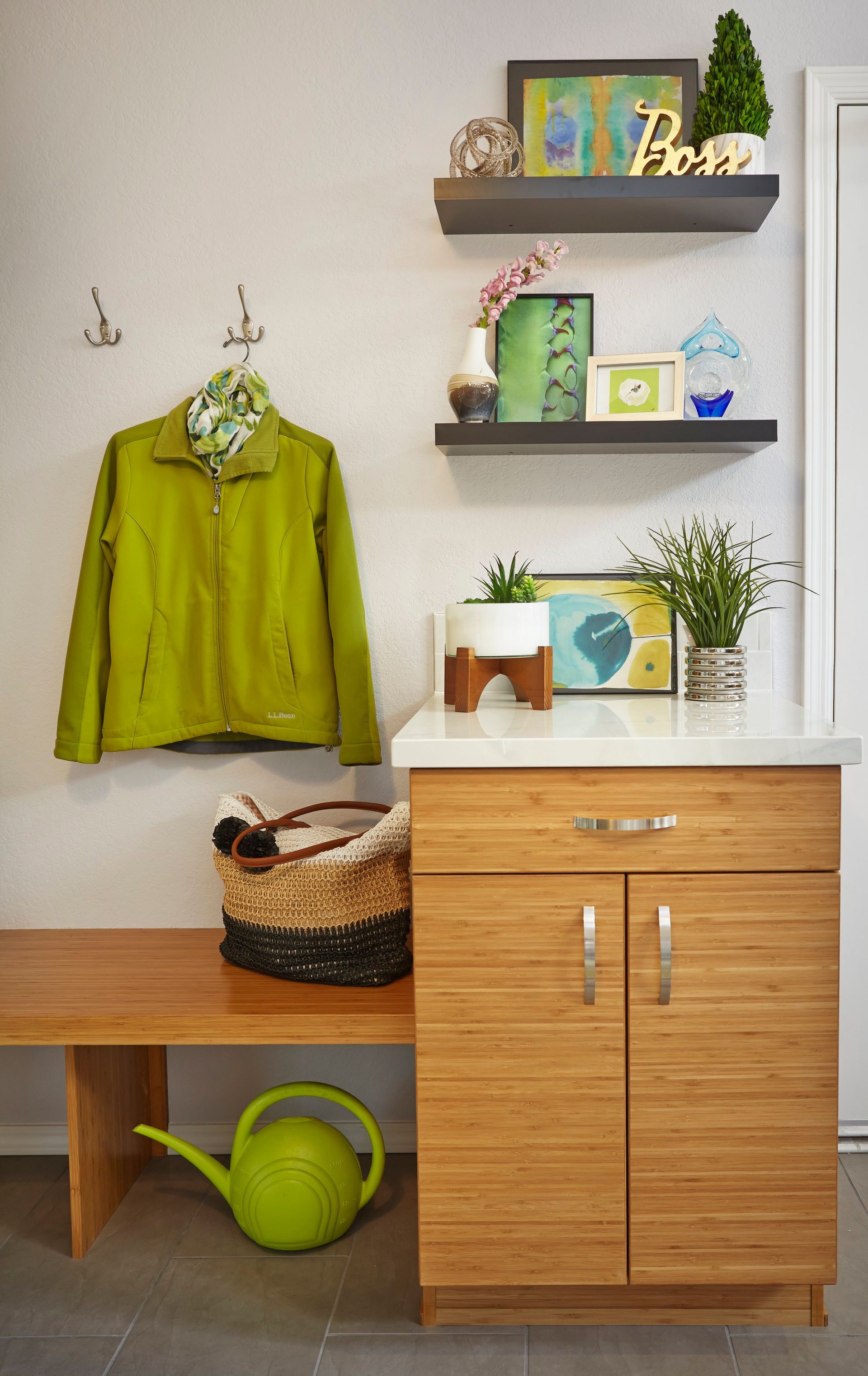 Mudroom with wood bench, cabinet, shelves, green jacket, watering can, and decor.