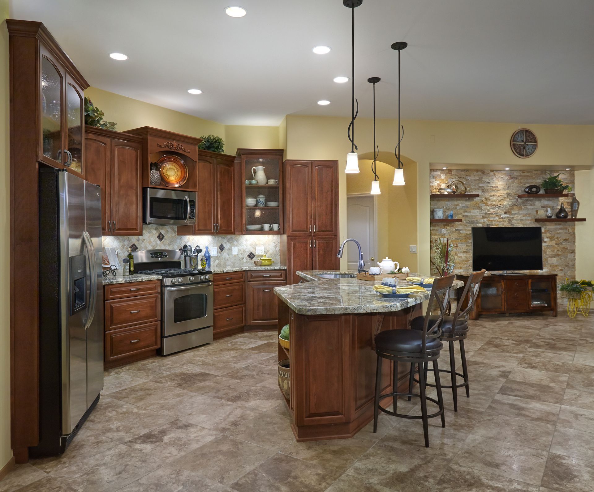 Kitchen with brown cabinets, island, stainless steel appliances, and stone tile flooring.
