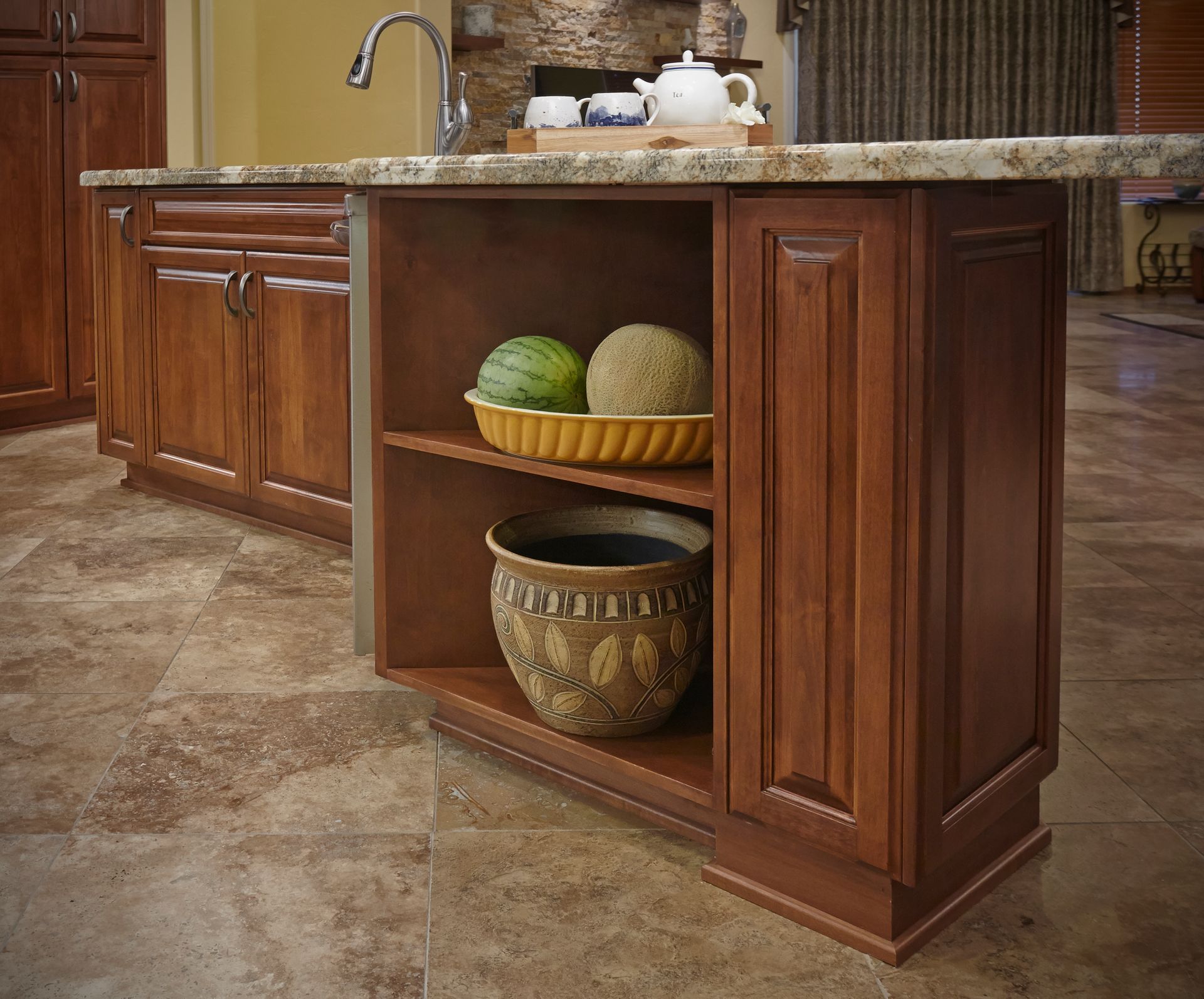 Kitchen island with open shelving and wooden cabinets.  Shelves hold fruit and a decorative pot.