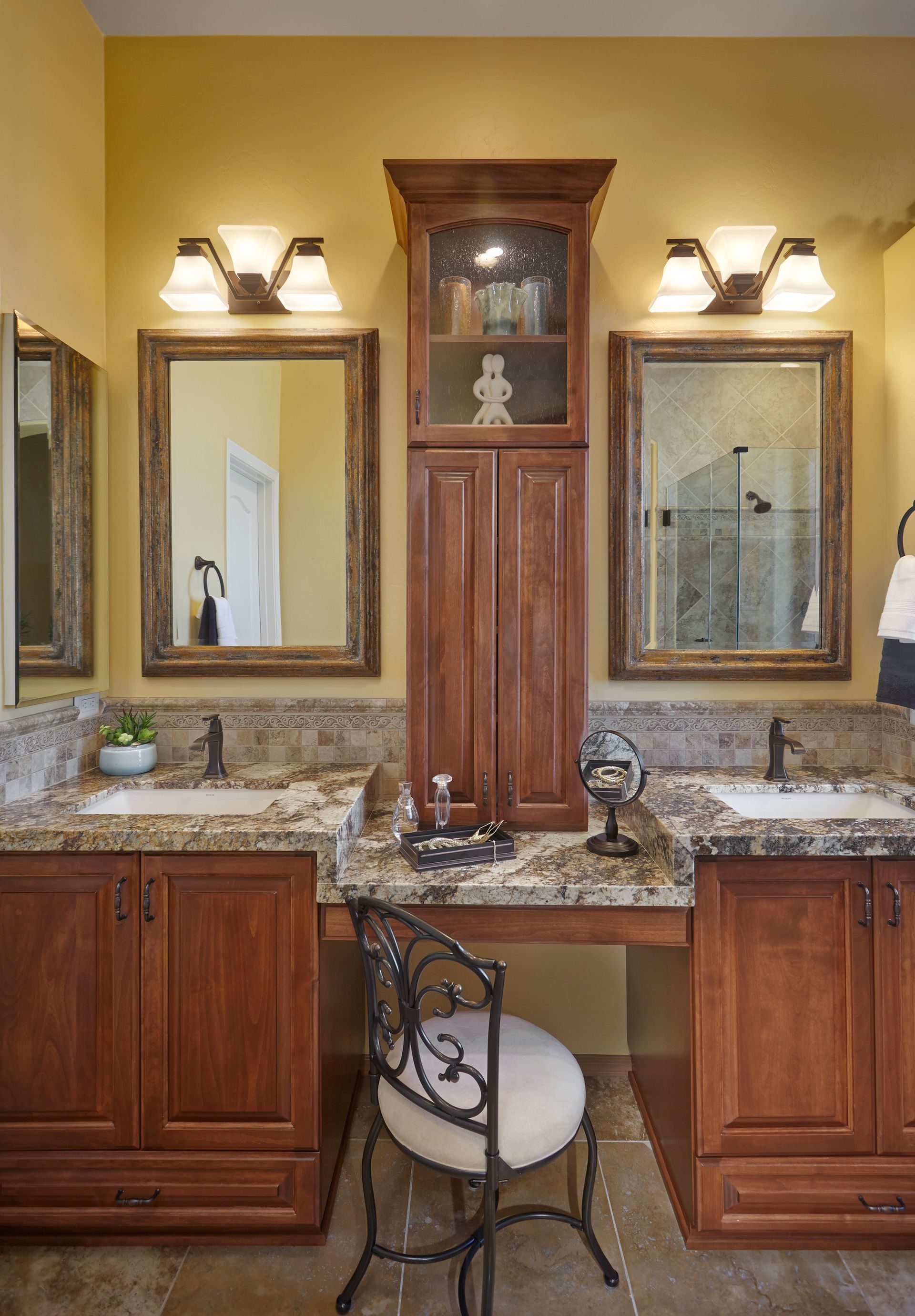 Bathroom with dual sinks, vanity area, wooden cabinets, mirrors, and a central storage cabinet.