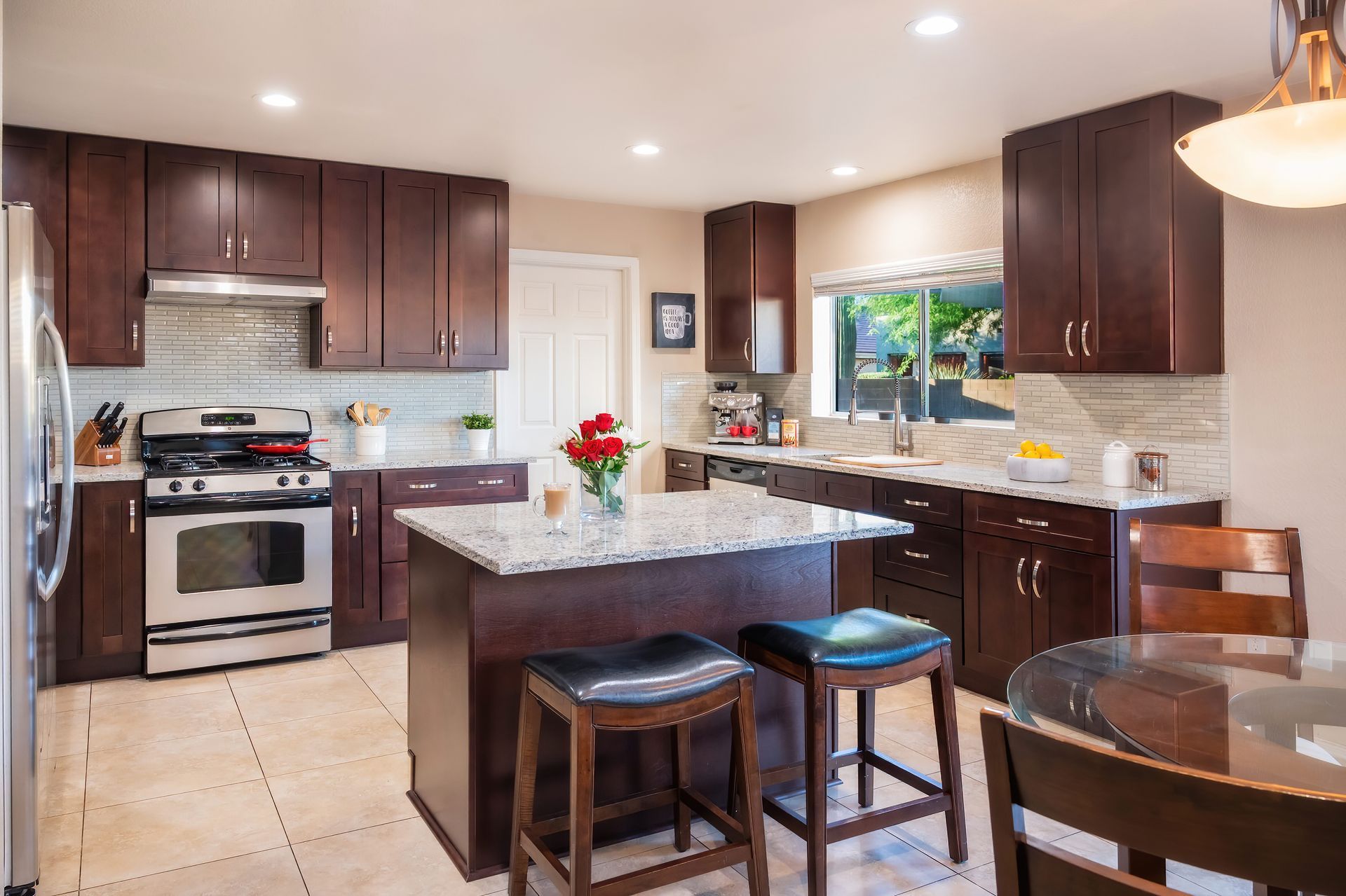 Kitchen with dark wood cabinets, stainless steel appliances, granite island, and dining table.