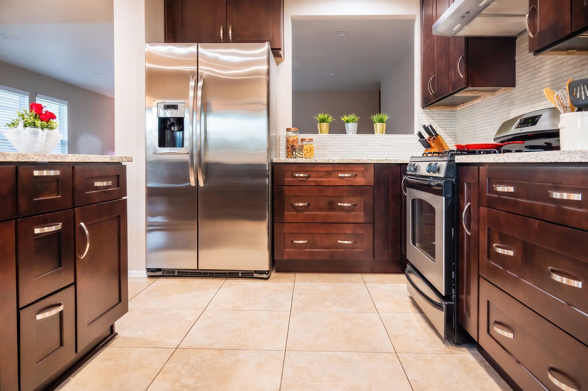 Kitchen with stainless steel refrigerator, dark wood cabinets, granite countertops, and tiled floor.