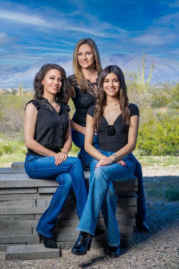 Three women are sitting next to each other on a brick wall.