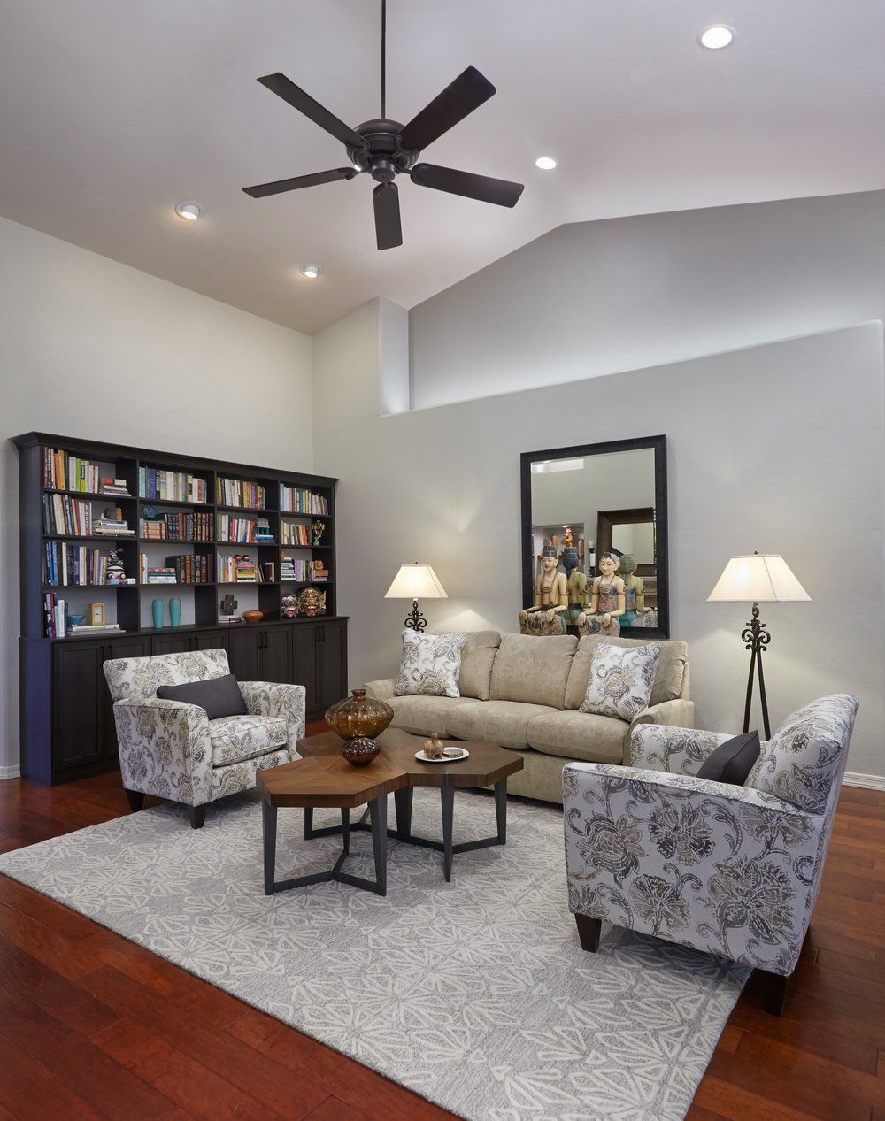 Living room with dark bookshelf, light gray walls, two patterned chairs, and a brown sofa.
