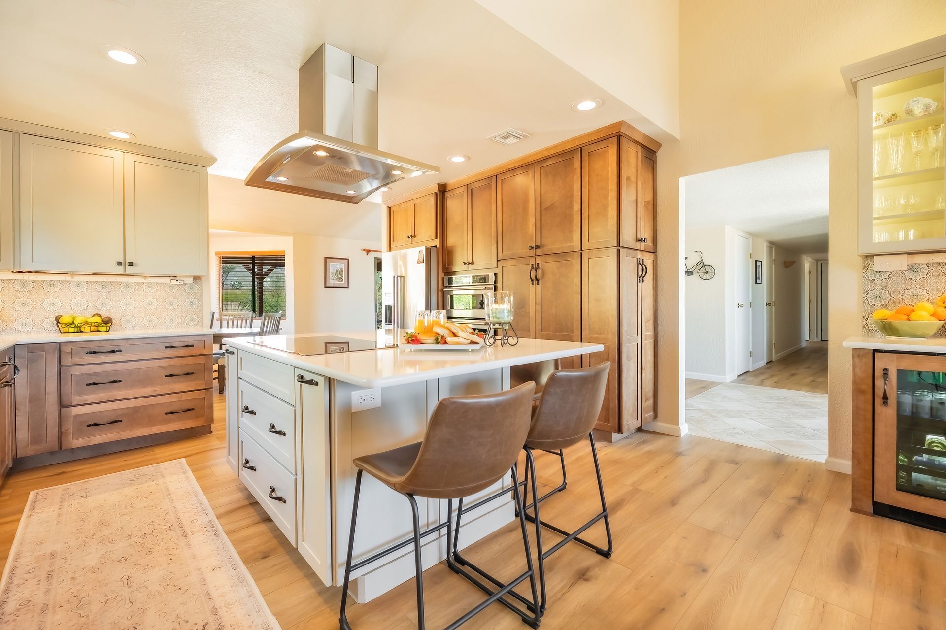 Kitchen with an island and bar stools; neutral tones with wood cabinets and flooring.