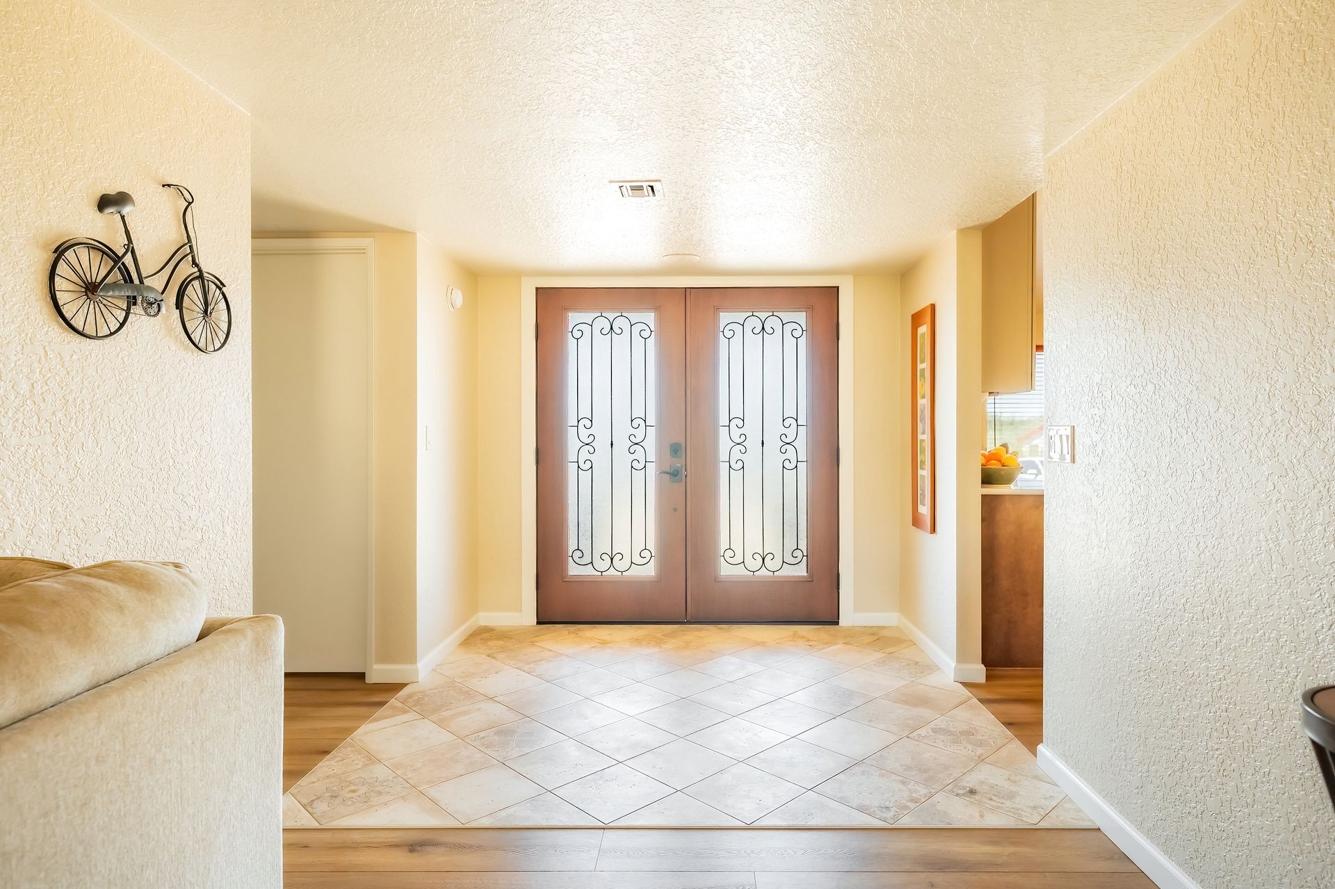 Entryway with double doors, patterned rug, wooden floors, and textured walls; decorative bicycle on wall.