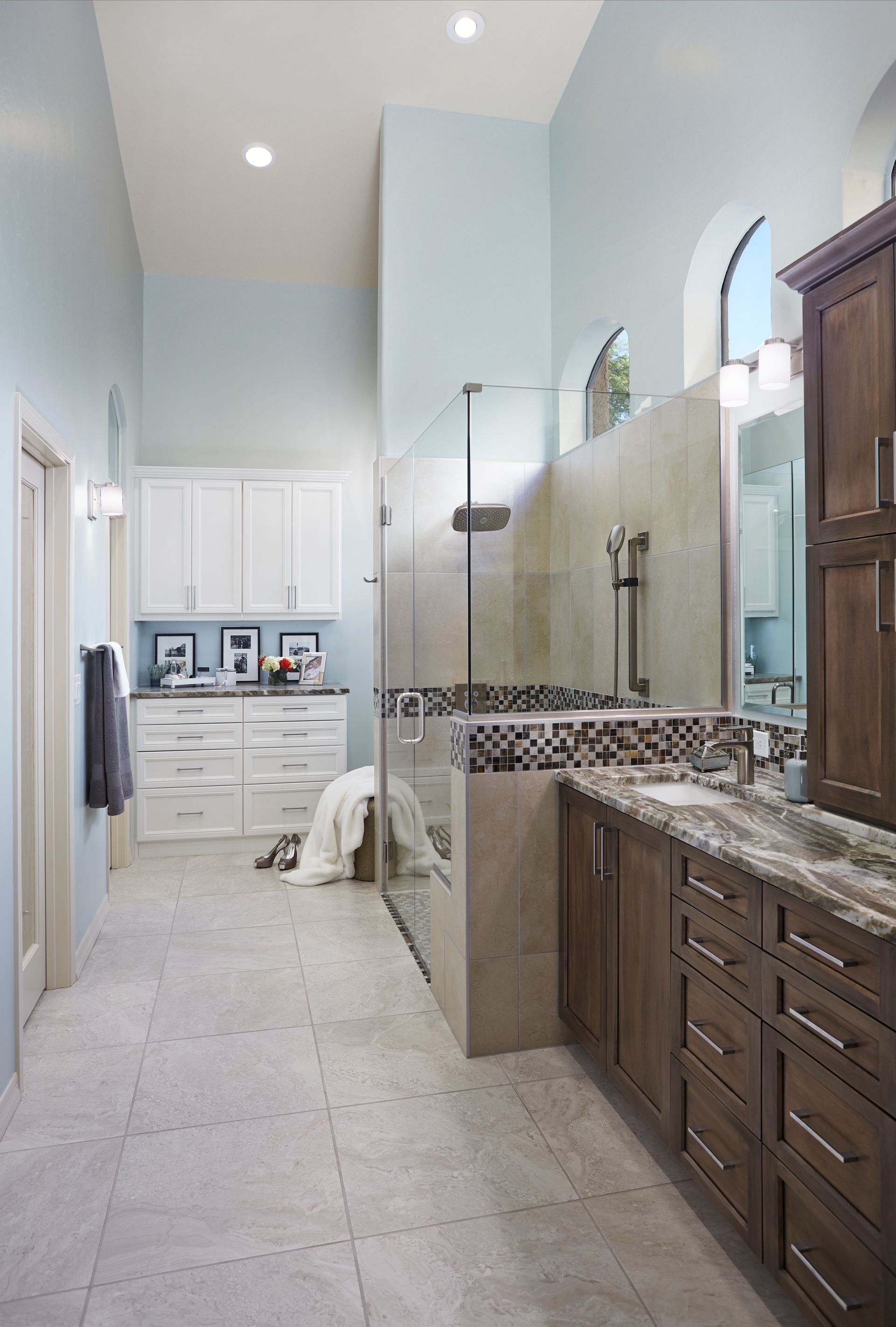 Spacious bathroom with tall ceilings, walk-in shower, dark wood vanity, light blue walls, and white cabinets.