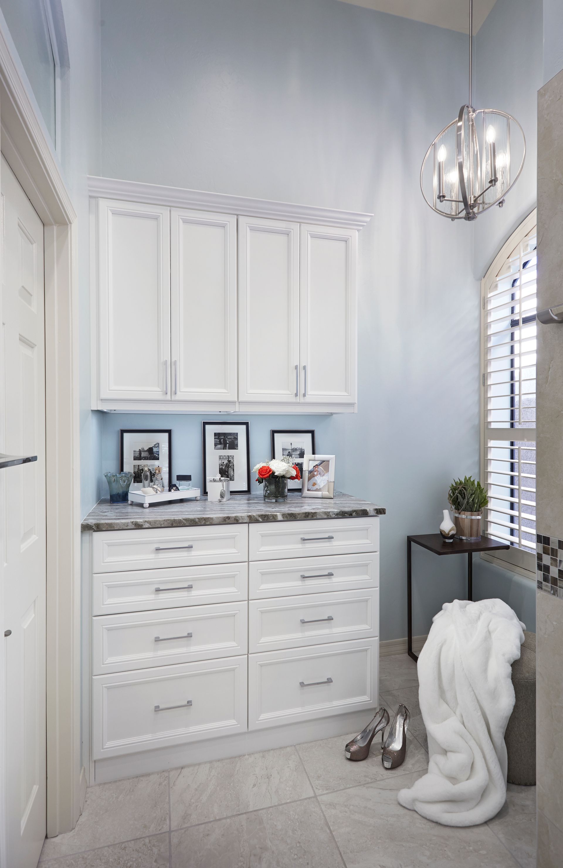 White cabinets in a light blue bathroom with a chandelier, and a rolled-up towel.