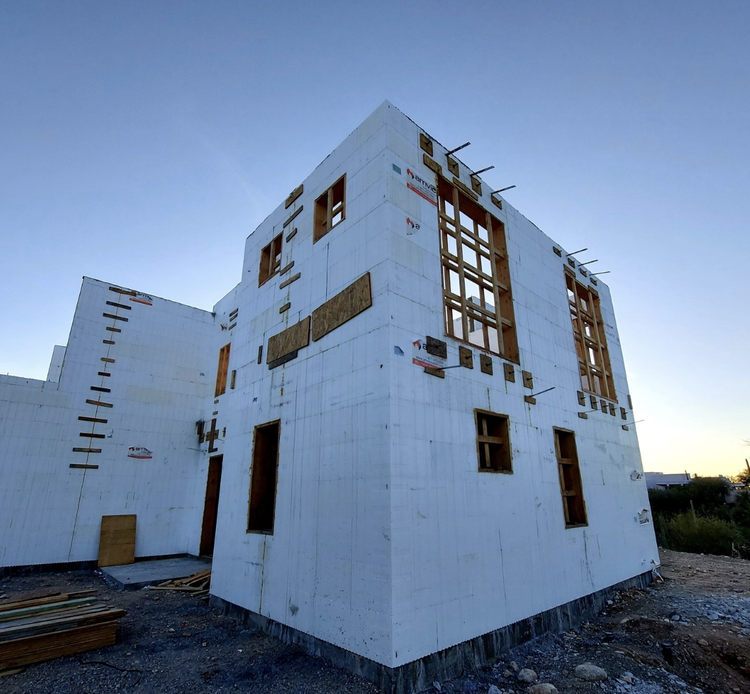 Exterior view of a two-story building under construction; white insulated concrete forms, window frames, and blue sky.