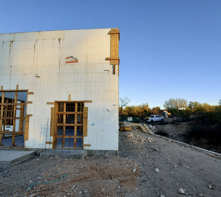 Construction site with white foam walls, window frames, and a truck parked nearby under a blue sky.