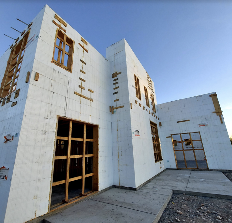 Exterior of a building under construction, white walls, wooden frames for windows and doors, blue sky.