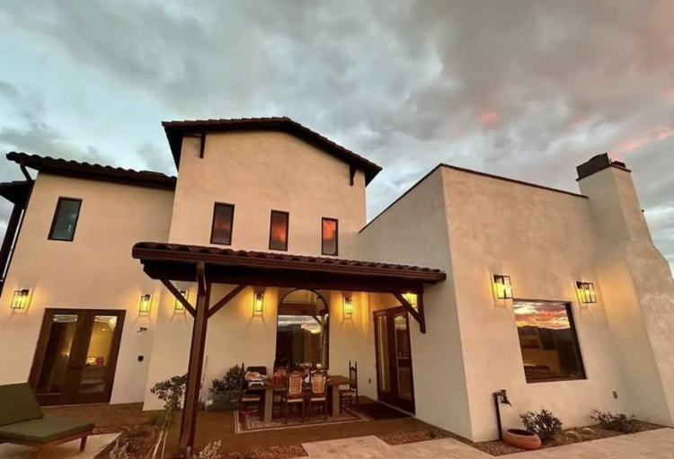 White stucco house with dark wood trim, an outdoor dining area, and a colorful sunset.