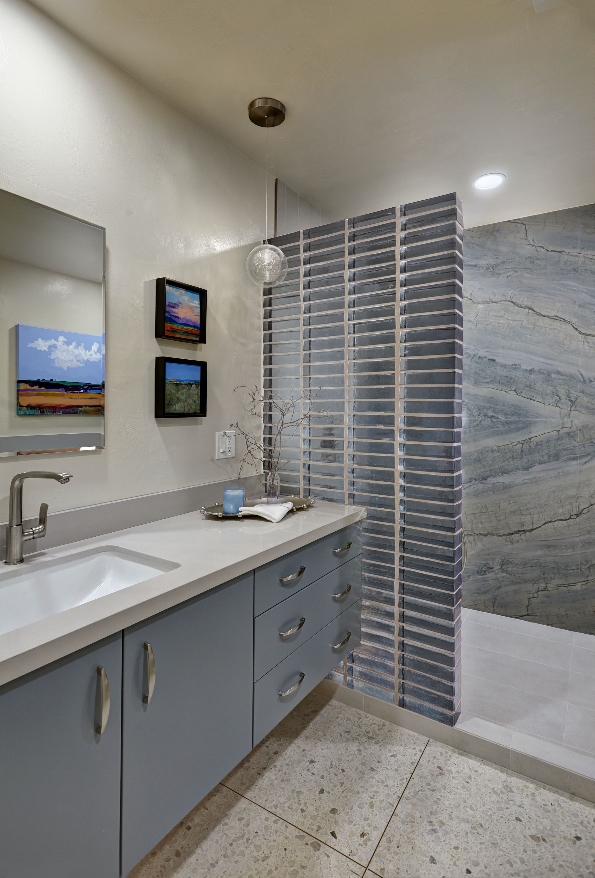 Bathroom with blue vanity, textured shower wall, and accent paintings.