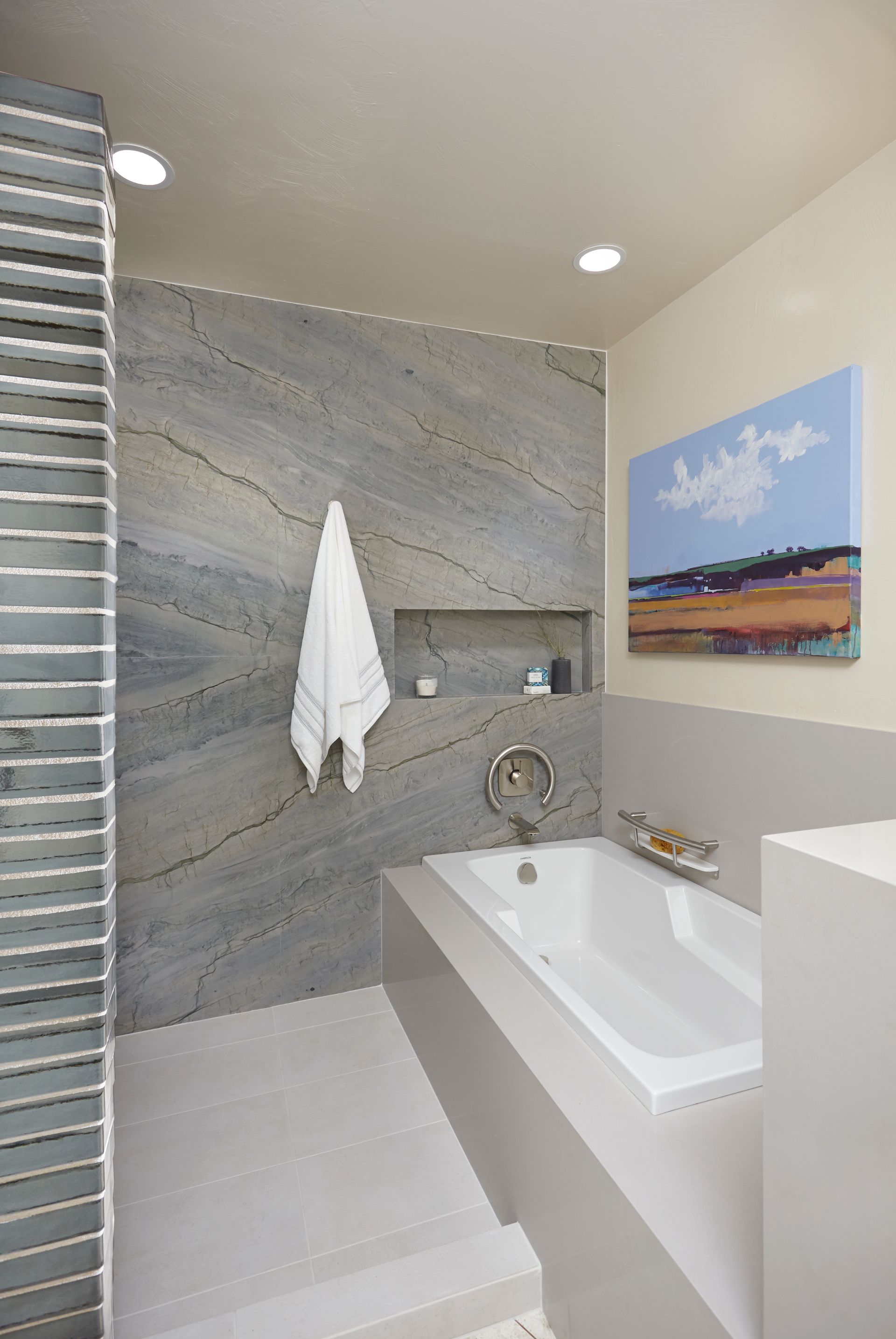 Modern bathroom with gray tile shower, built-in tub, and painting on the wall.