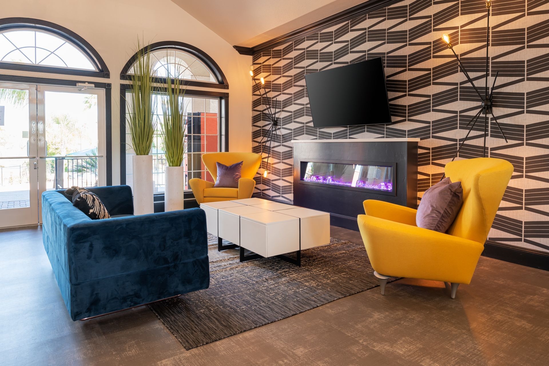 Lounge area with blue couch, yellow chairs, patterned wallpaper, fireplace, and TV.